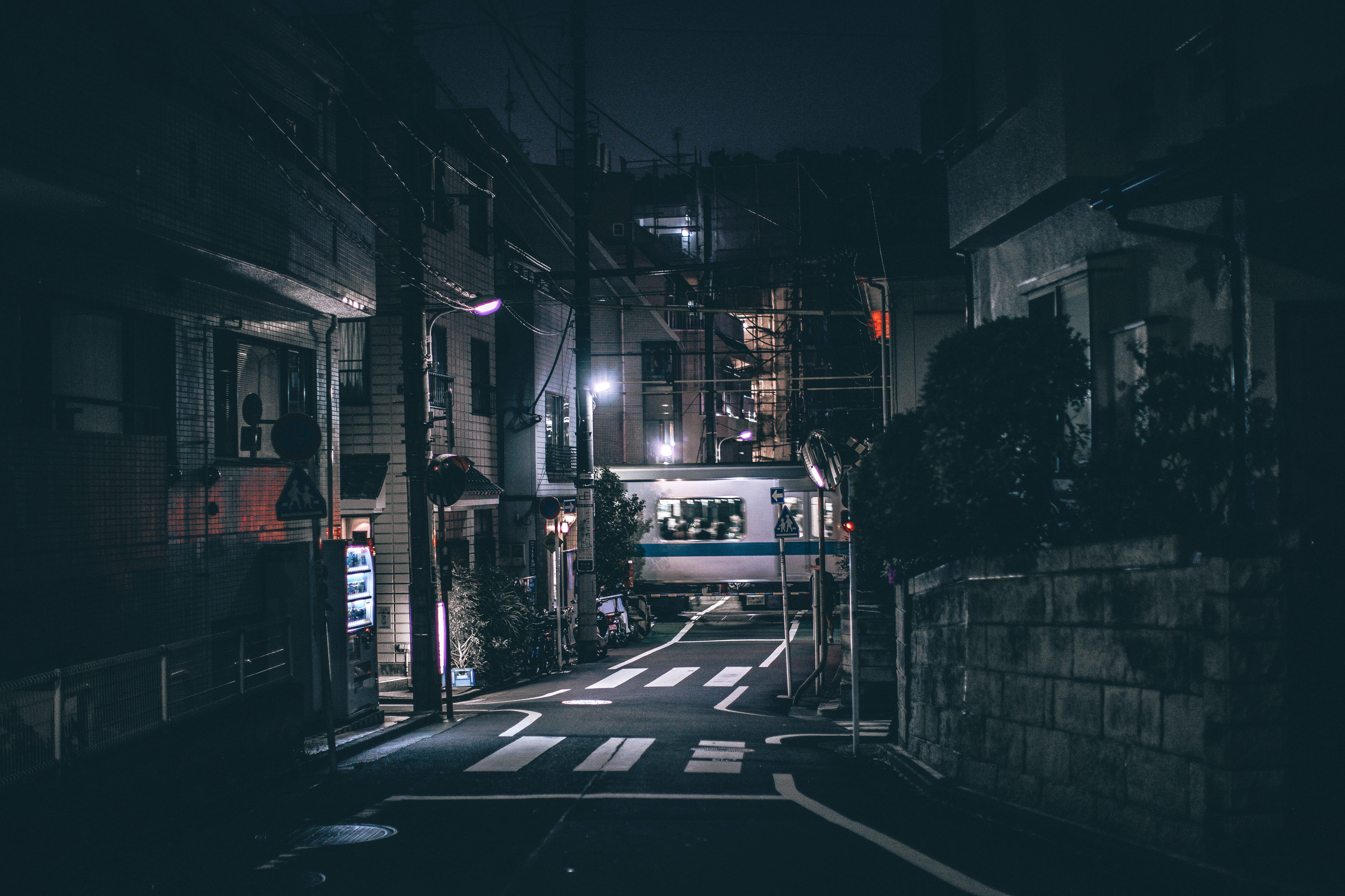 暗色 4K 桌布 壁紙 — 夜晚一條狹窄的日本街道，被街燈和一列經過的火車照亮，在濕漉漉的路面上投下倒影。