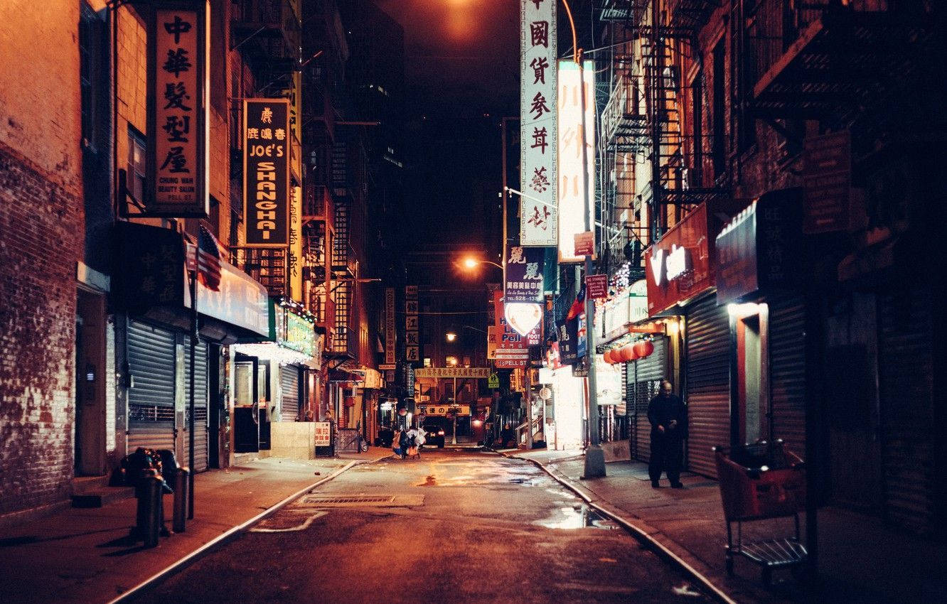 Chinatown 桌布 壁紙 — 夜晚一條狹窄的霓虹燈小巷，有發光的招牌和潮濕的路面反射著溫暖的橙色燈光。