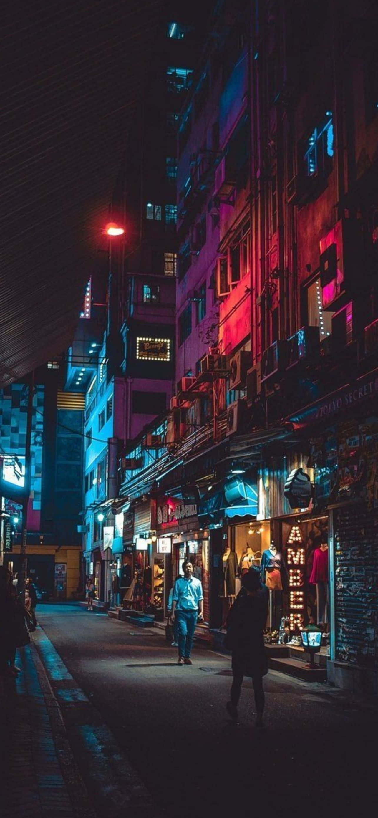 酷炫iPhone 桌布 壁紙 — 夜晚一條狹窄的霓虹燈小巷，行人走過色彩繽紛的商店櫥窗，頭頂是漆黑的天空。