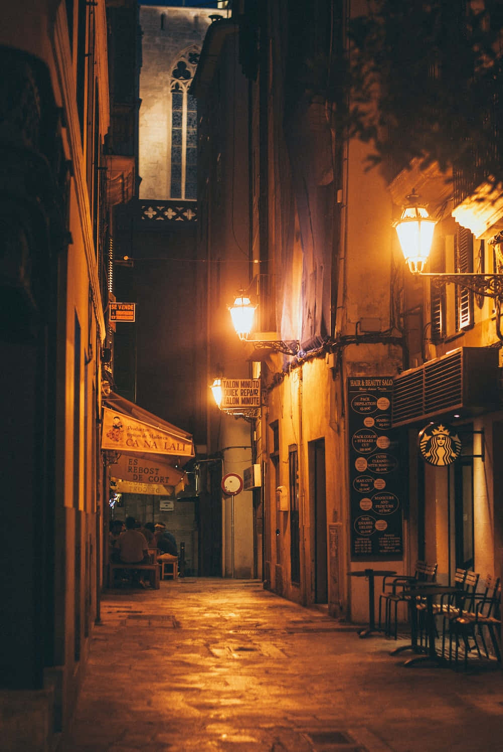 Night Street 桌布 壁紙 — 夜晚一條狹窄的鵝卵石小巷，沐浴在復古街燈和咖啡館招牌散發的溫暖金色光芒中。