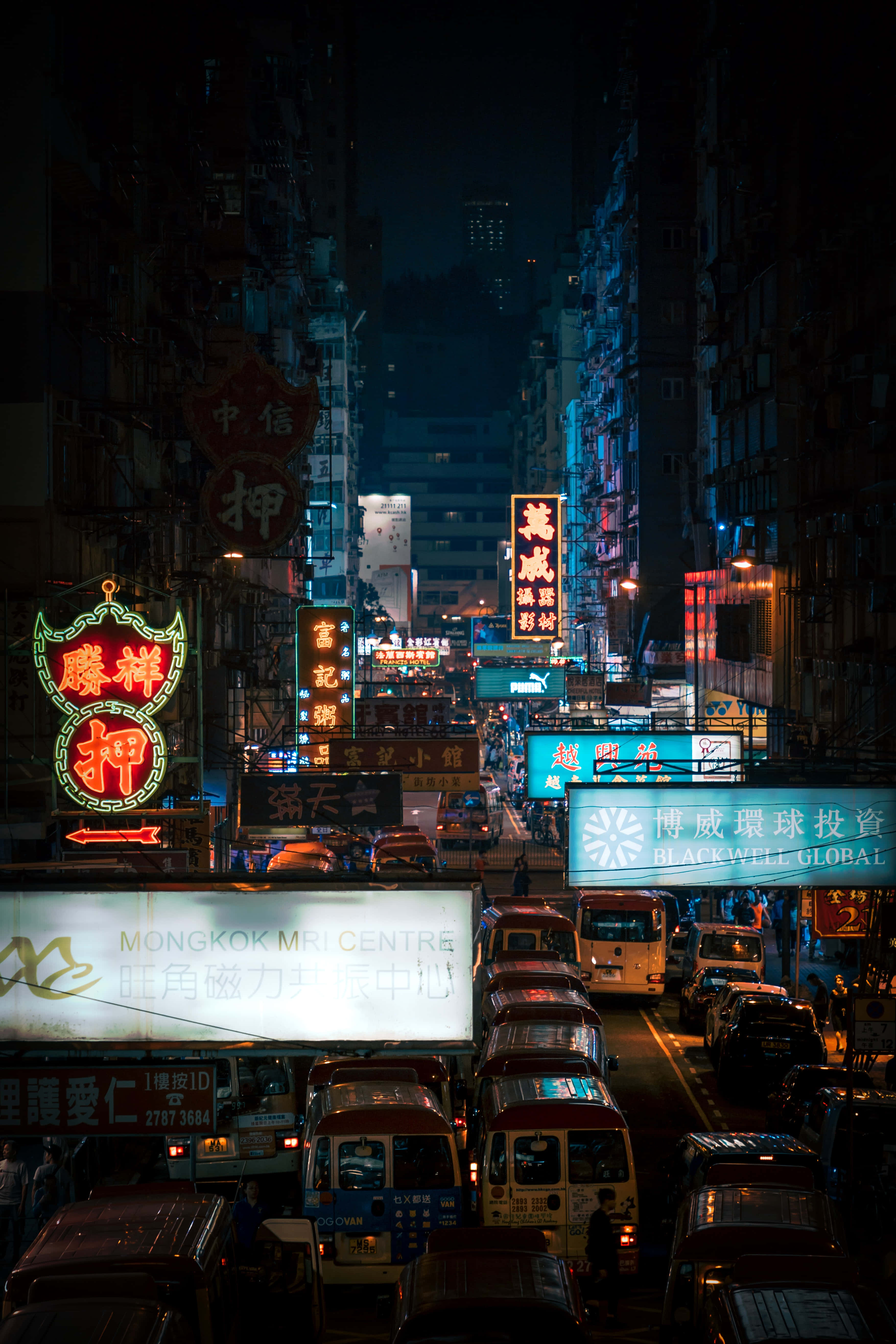 香港 桌布 壁紙 — 夜晚一條繁華的霓虹燈城市街道，高樓大廈、發光招牌和車水馬龍的道路。