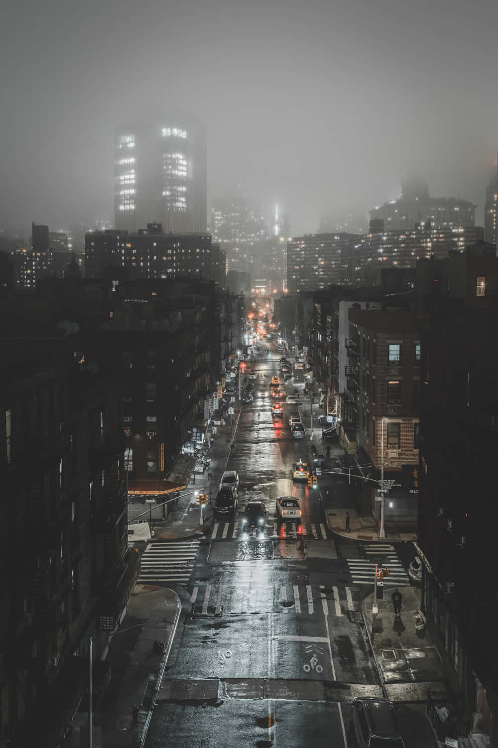 City At Night 桌布 壁紙 — 夜晚一條被雨水打濕的城市街道，閃爍的車頭燈和遠處被霧籠罩的摩天大樓。