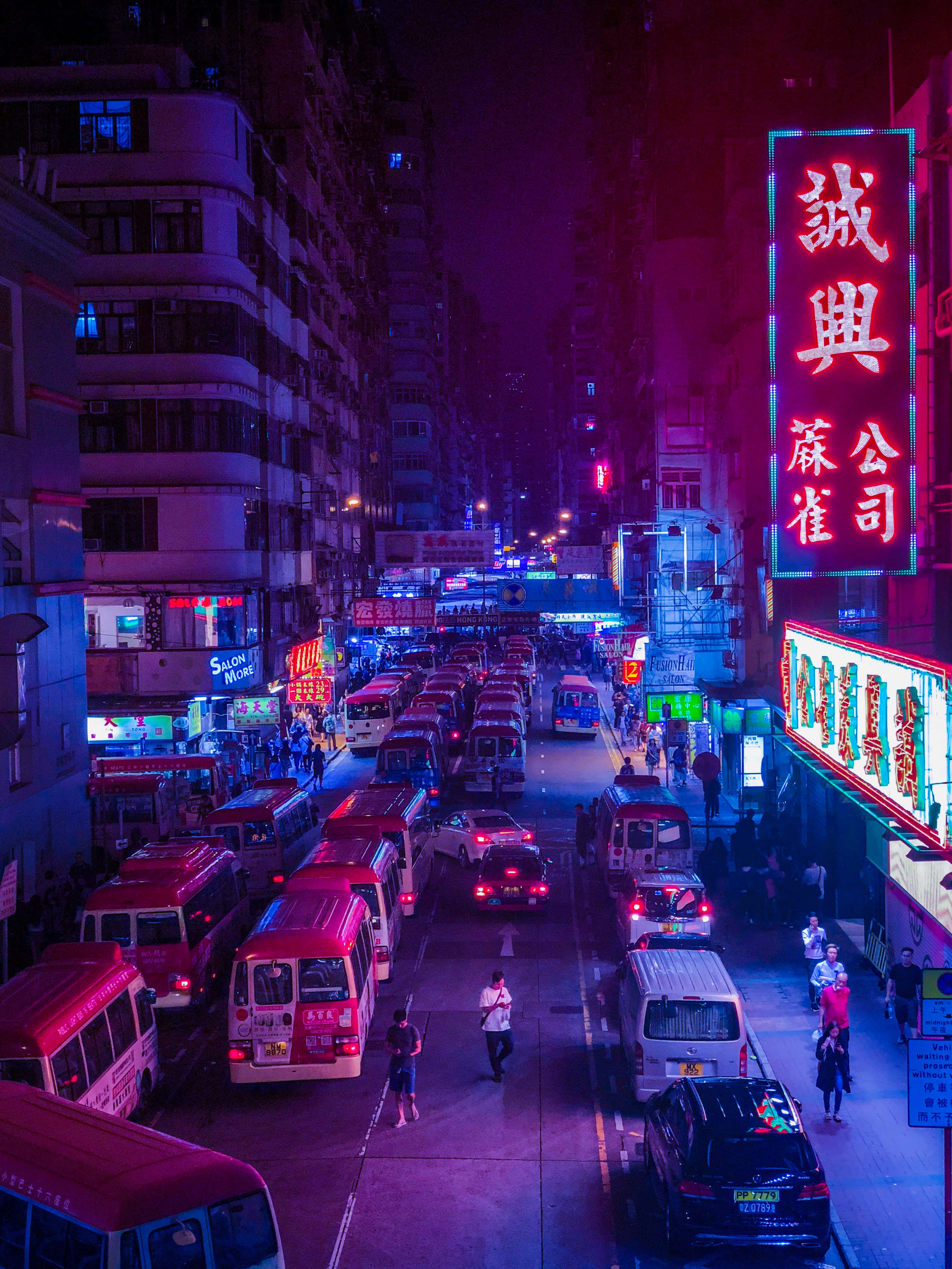 Hong Kong 桌布 壁紙 — 夜晚一條被霓虹燈浸染的城市街道，紅色巴士和發光招牌在擁擠的人行道上投射出鮮豔的紫色和粉紅色光芒。