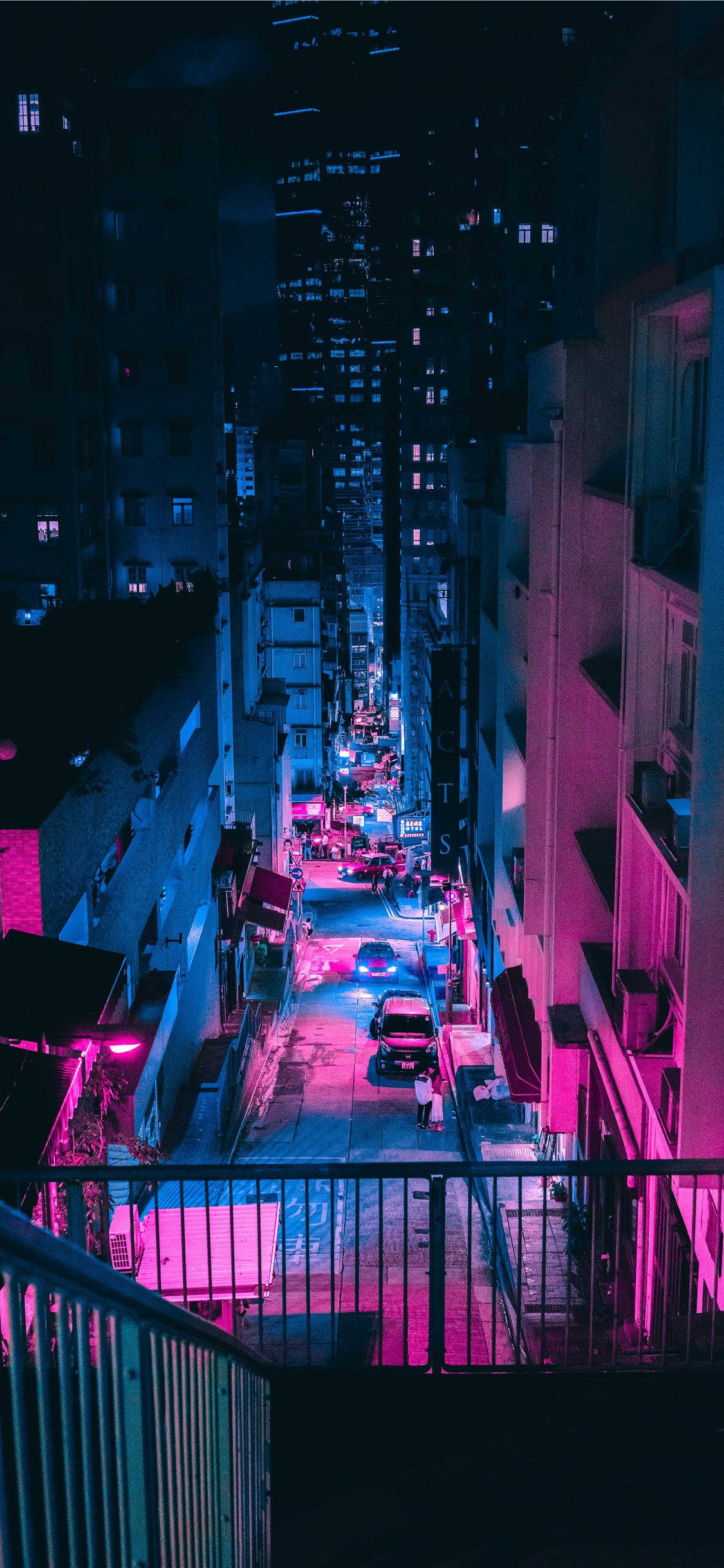 手機 桌布 壁紙 — 夜晚一條被霓虹燈浸透的城市小巷，粉紅色和藍色的燈光在潮濕的路面和高聳的建築物上反射。