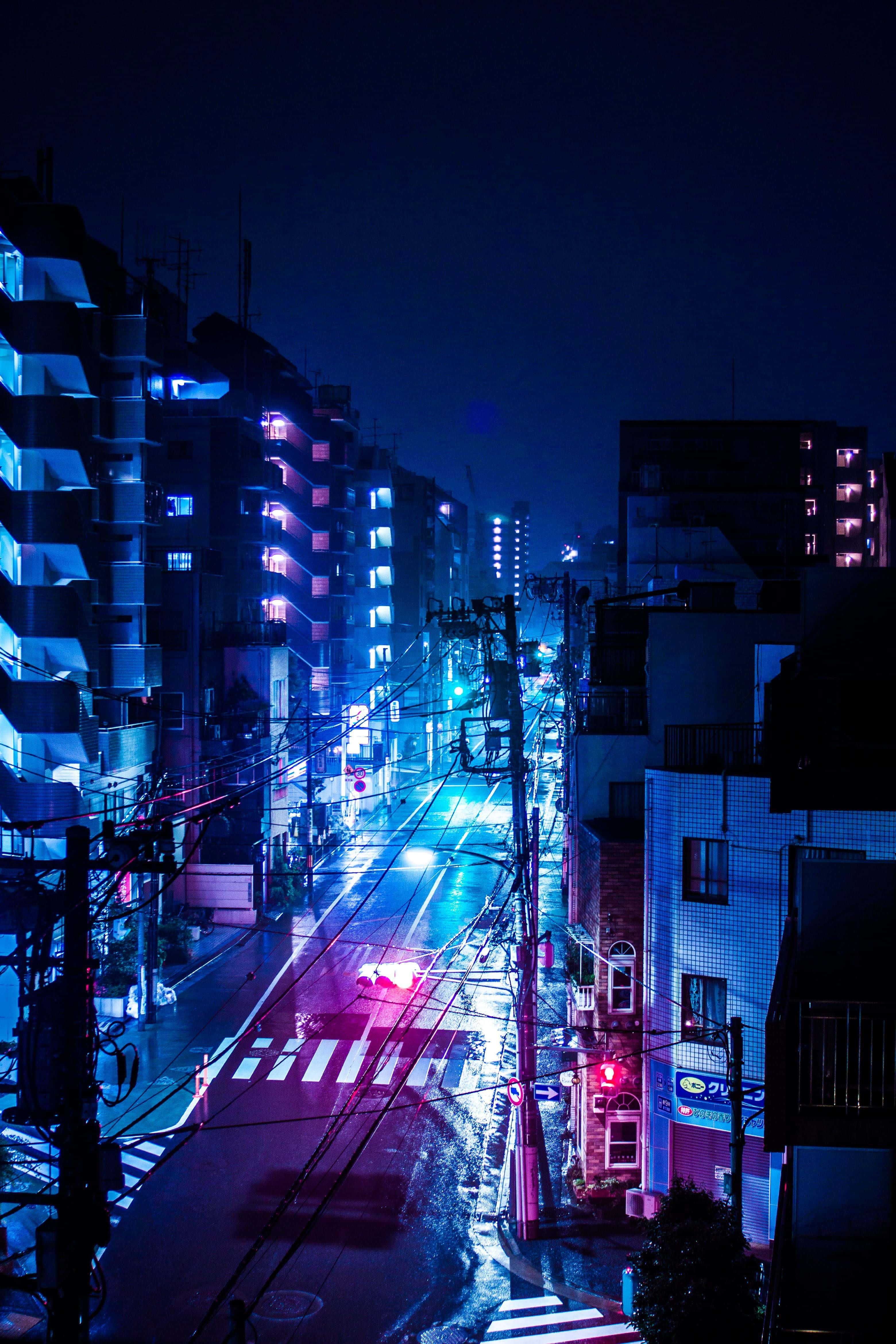 Neon City Aesthetic 桌布 壁紙 — 夜晚一條被霓虹燈浸透的城市街道，潮濕的路面反射著建築物和汽車的藍色和粉紅色燈光。