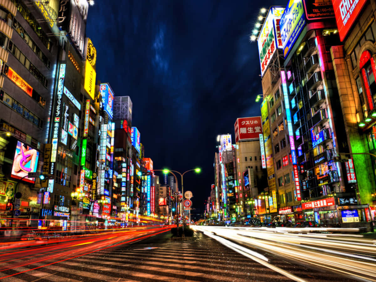 Tokyo Night 桌布 壁紙 — 夜晚一條閃爍霓虹燈光的城市街道，車流留下光軌，高樓大廈閃爍著鮮豔的招牌。