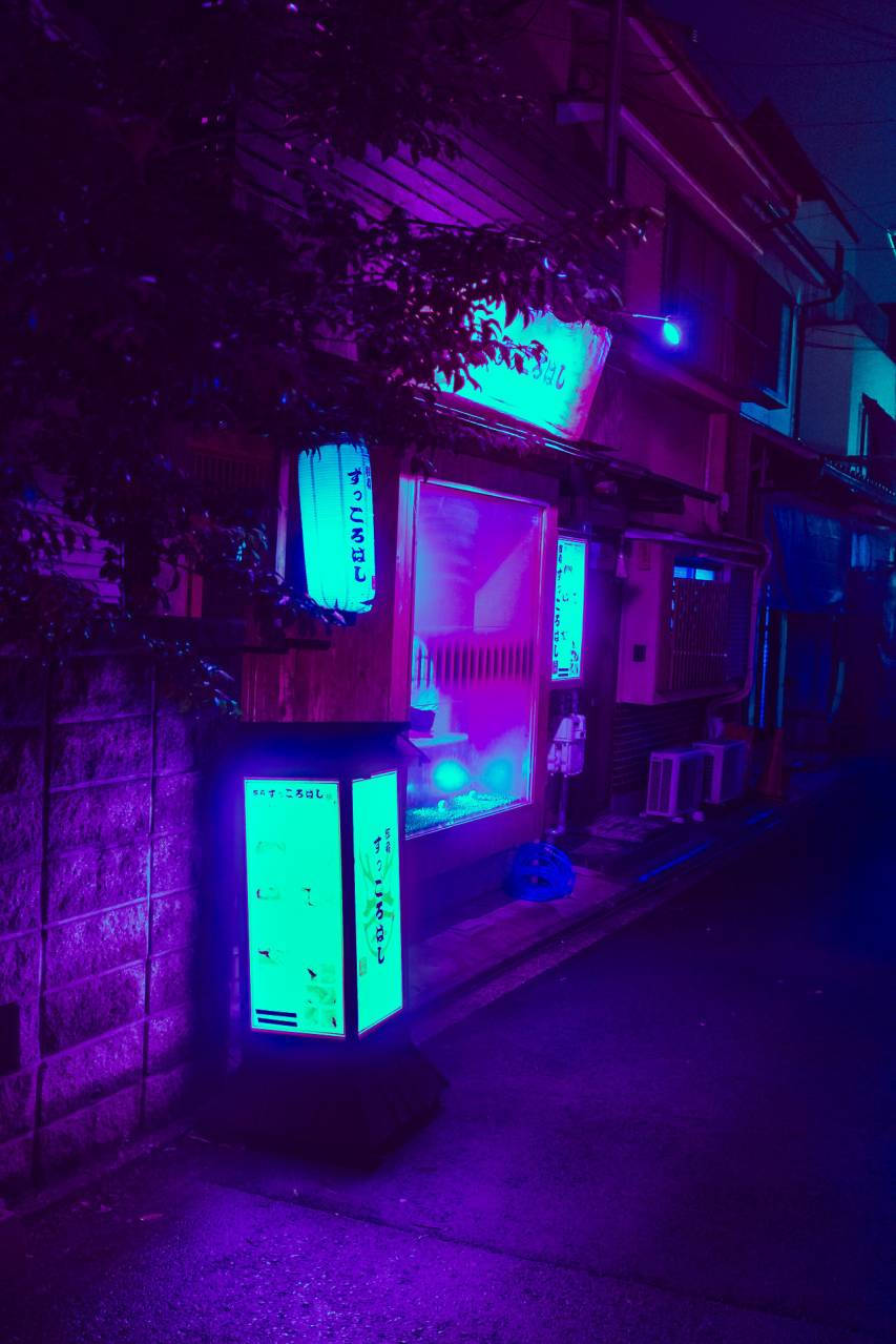 dark neon iPhone 桌布 壁紙 — 夜晚一條霓虹燈照亮的日本小巷，綠色發光的自動販賣機和紫色環境光在石牆和樹木上投下陰影。