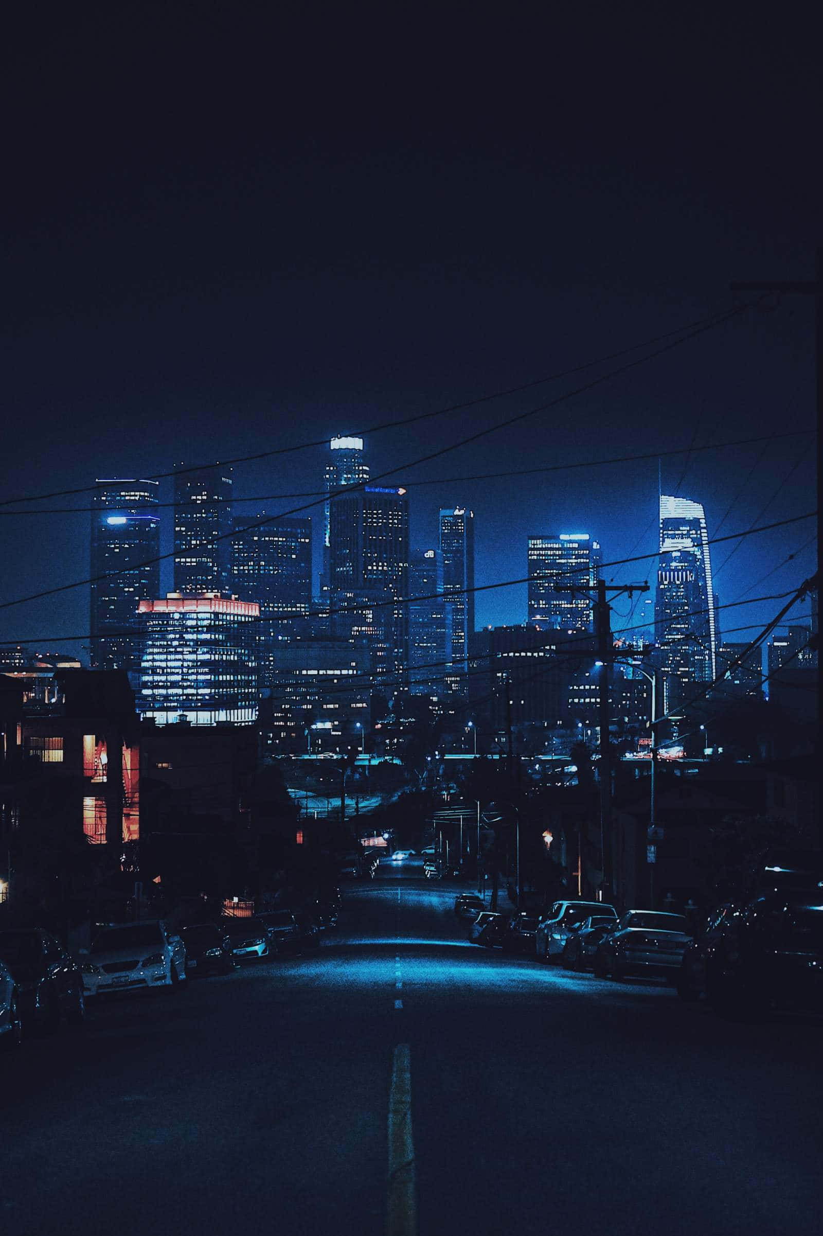 Dark Crossroad 桌布 壁紙 — 夜晚一條黑暗的城市街道通向閃爍著藍色和橙色燈光的城市天際線。