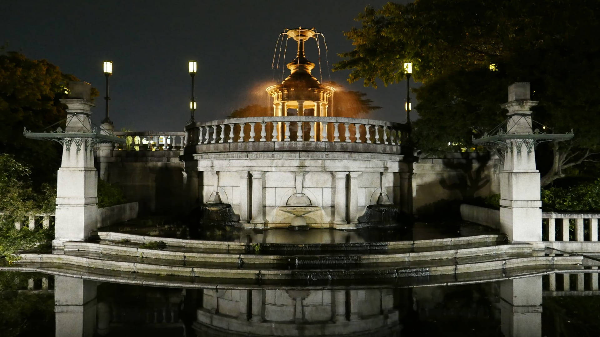 Nagoya 桌布 壁紙 — 夜晚中一座宏偉的照明噴泉，水流沿石階傾瀉而下，在平靜的池塘中倒映，周圍環繞樹木。