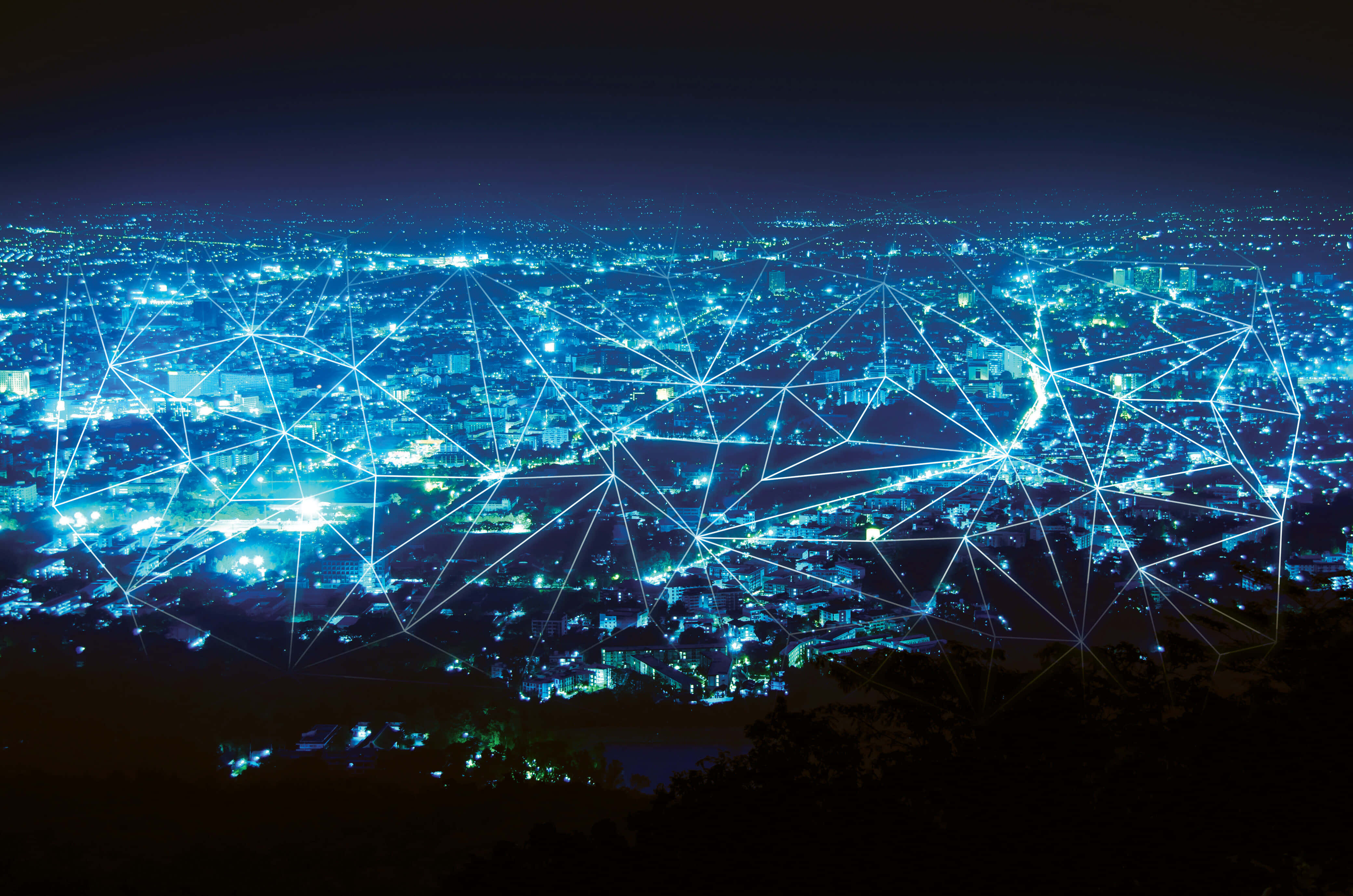 Internet 桌布 壁紙 — 夜晚中一座廣闊的城市被發光的藍色燈光照亮，並有數位網路覆蓋層連接建築物和街道。