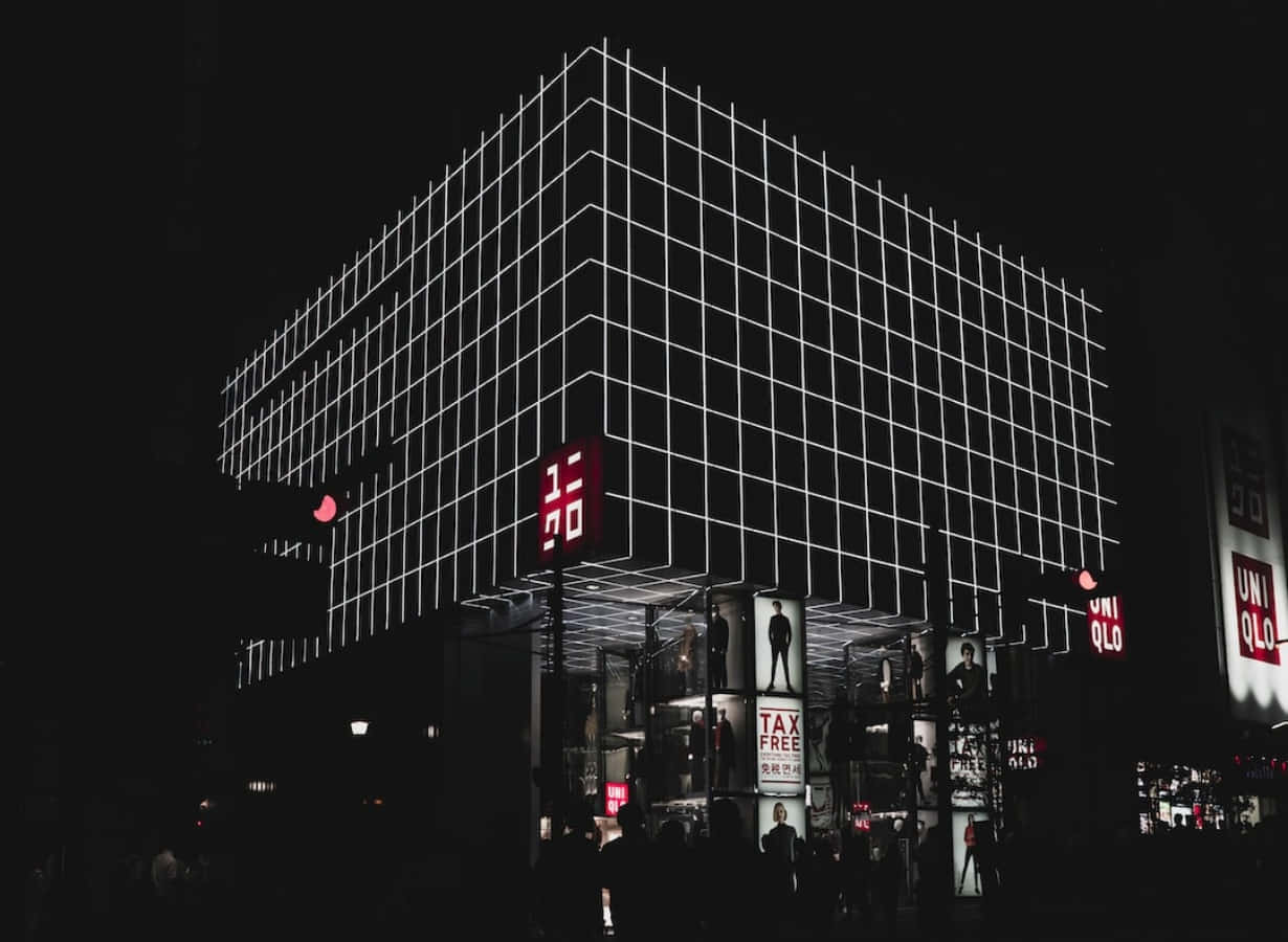 Uniqlo 桌布 壁紙 — 夜晚中一座引人注目的幾何建築，發光的白色網格線和紅色Uniqlo標誌在黑暗的天空下格外醒目。