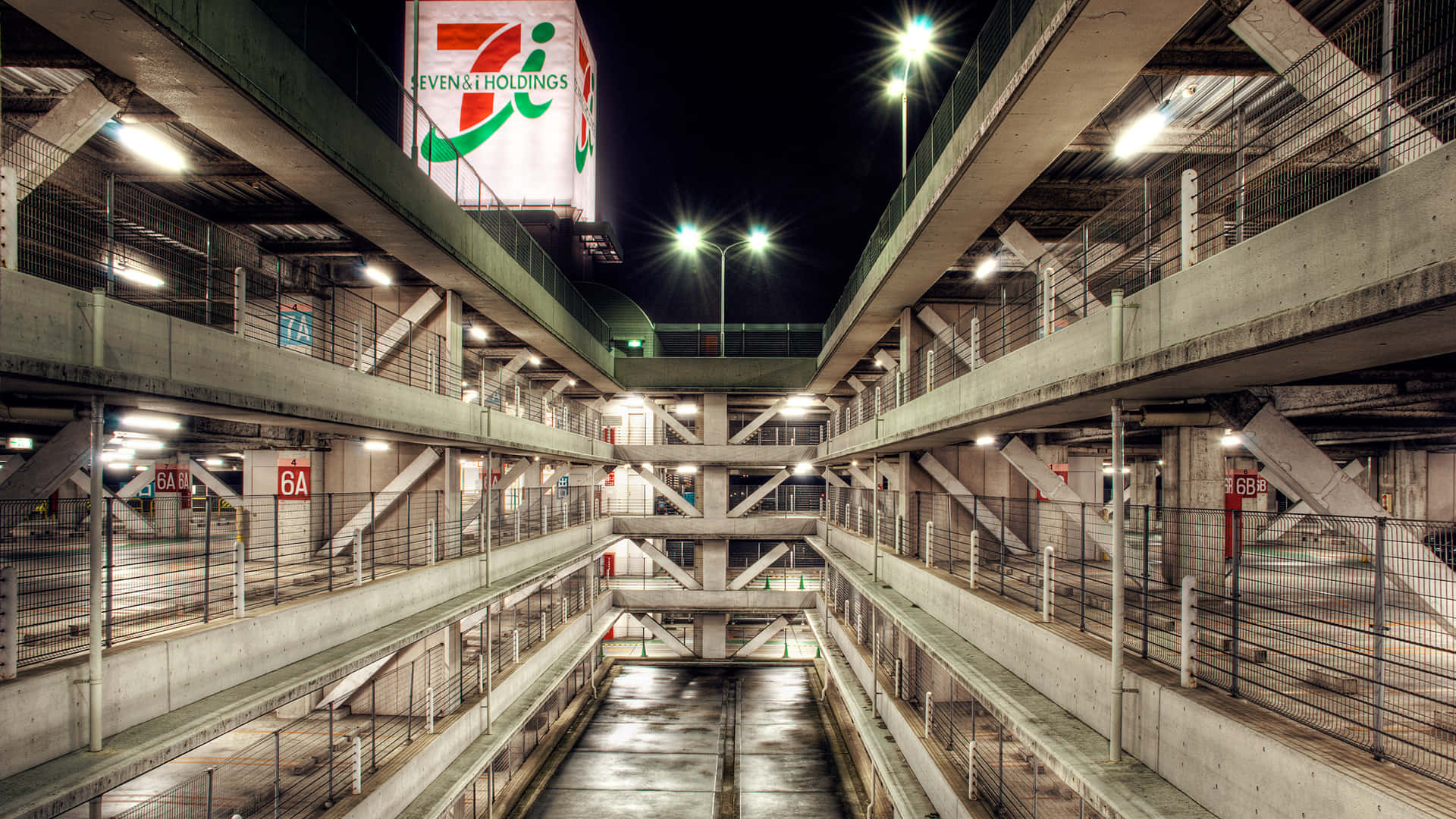 Building 桌布 壁紙 — 夜晚中一座高聳的混凝土停車場被人工燈光照亮，上方有一個大型7-Eleven標誌發光。