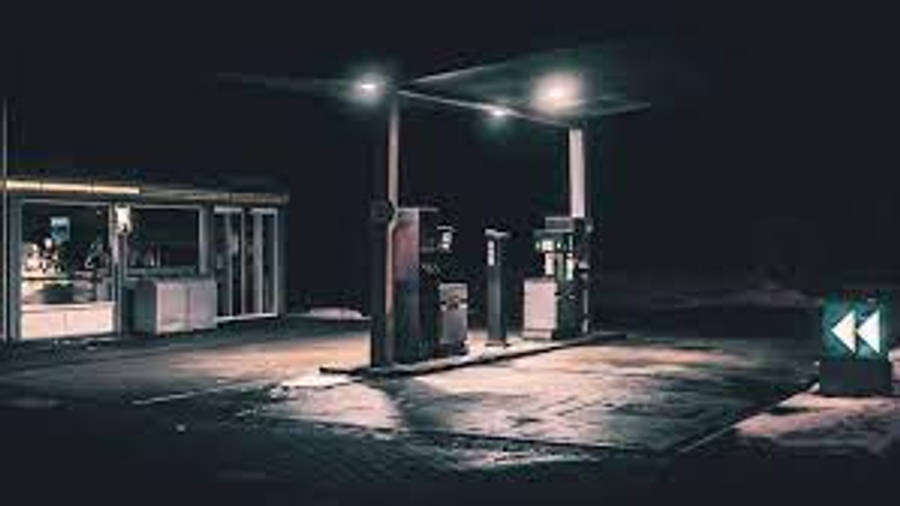 Gas 桌布 壁紙 — 夜晚中孤獨的加油站，被刺眼的頭頂燈照亮，在濕漉漉的路面上投下長長的影子。