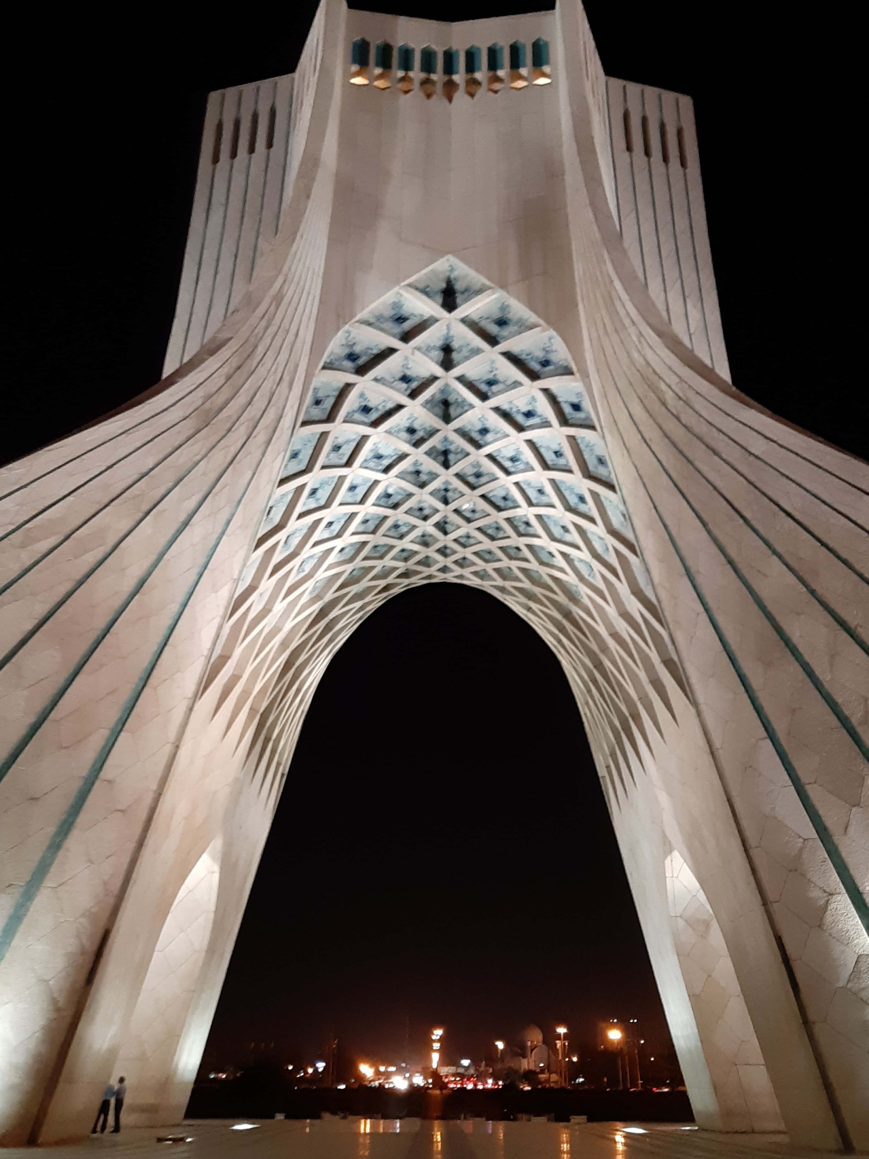 Tehran 桌布 壁紙 — 夜晚中宏偉的照明拱門，帶有複雜的幾何圖案，通過開口可見城市景觀。