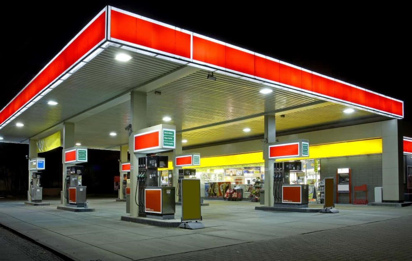 Petrol Station 桌布 壁紙 — 夜晚中明亮照明的加油站，紅色和黃色的標誌在黑暗的天空下發光。