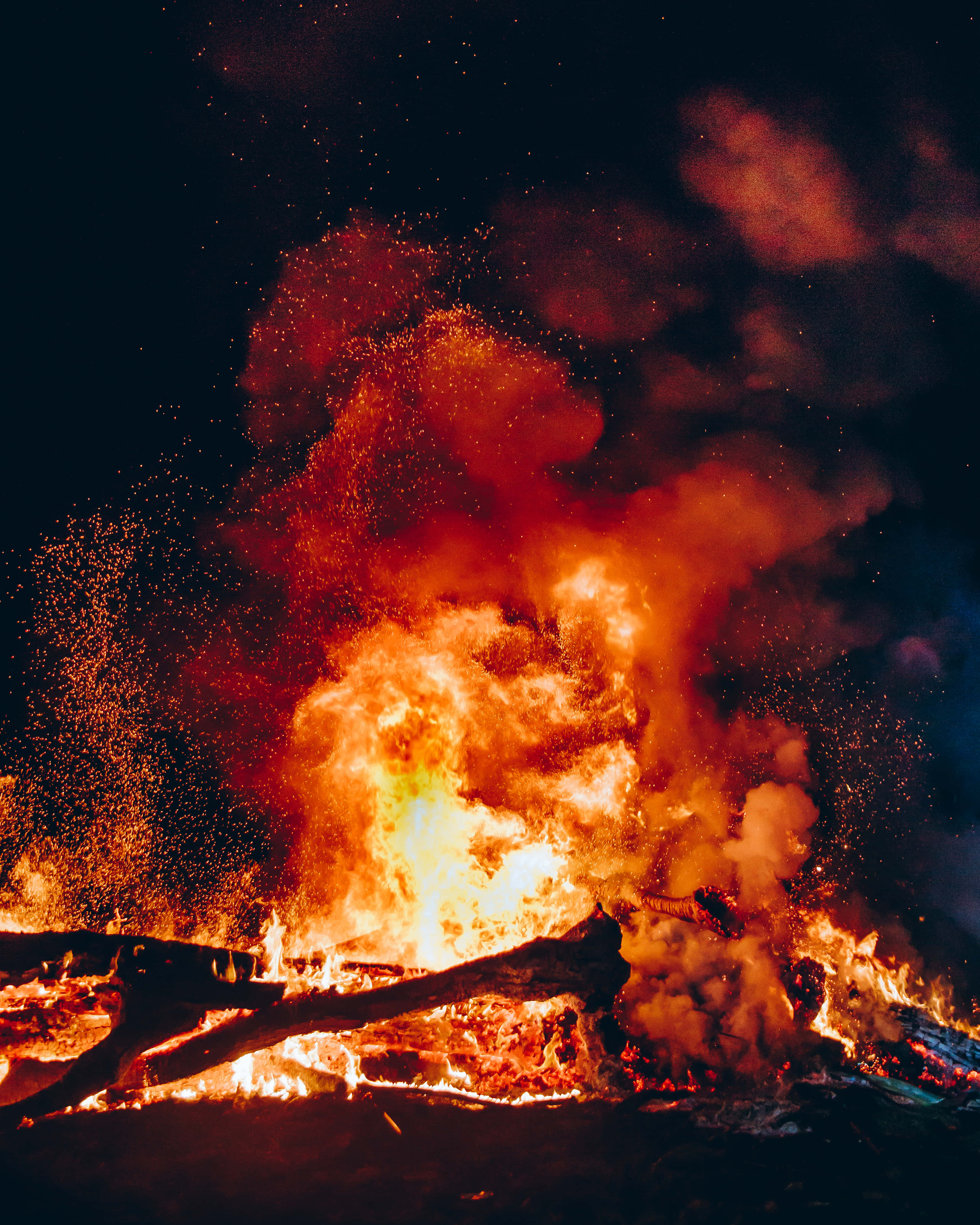 Burn 桌布 壁紙 — 夜晚中熊熊燃燒的營火，明亮的橙色火焰和發光的餘燼映襯著黑暗的天空。