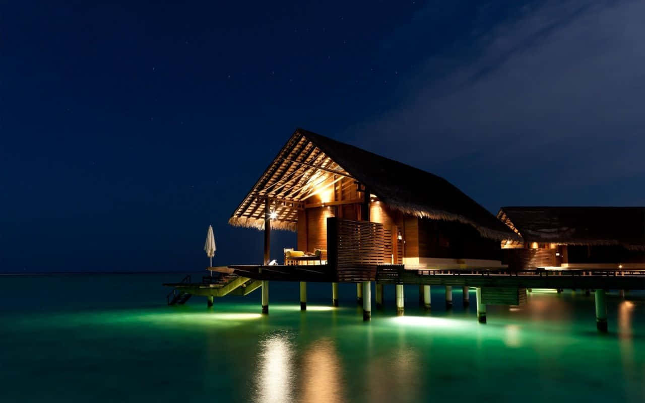 1280x800 桌布 壁紙 — 夜晚中發光的水上平房，溫暖的燈光在星空下反射在碧綠色的水面上。