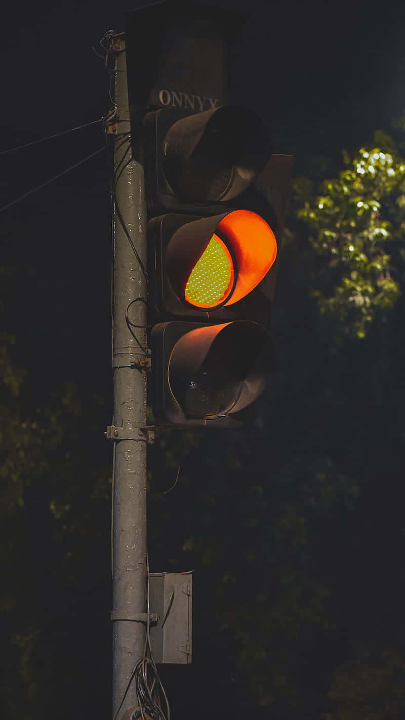 Light 桌布 壁紙 — 夜晚交通號誌的特寫，琥珀色的燈光在黑暗背景和模糊的綠色樹葉中溫暖地發光。
