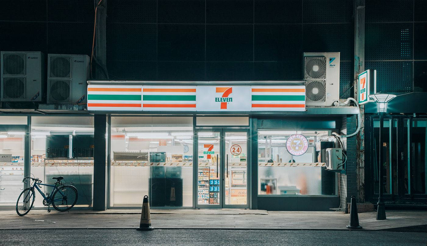 Store 桌布 壁紙 — 夜晚亮燈的7-Eleven商店，外面停著一輛腳踏車，上方裝有空調。