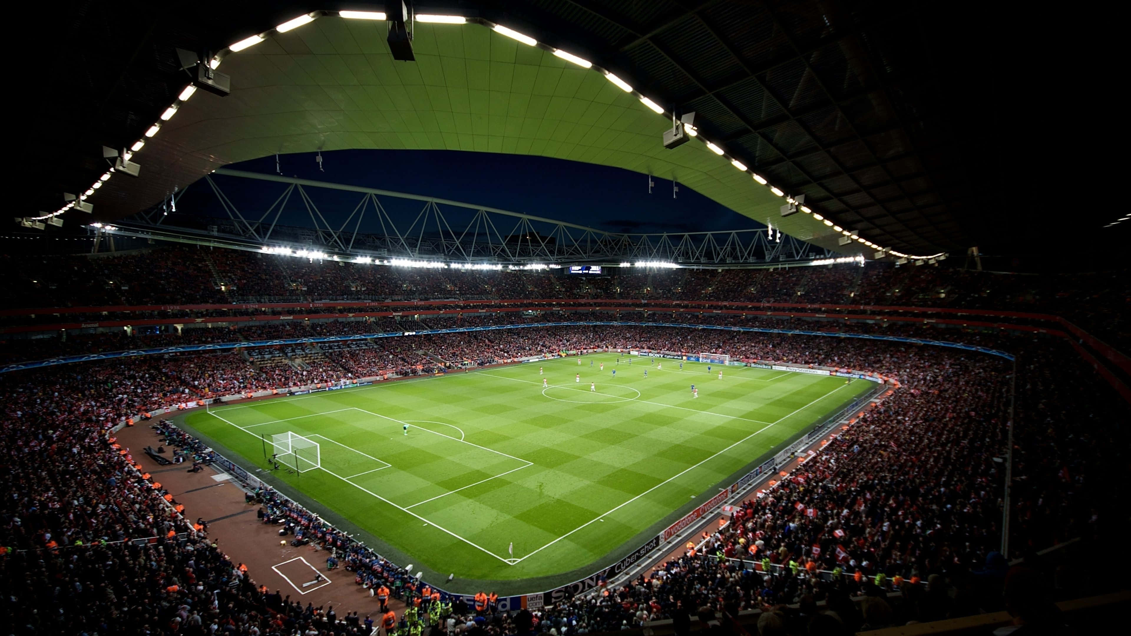 Soccer 4K 桌布 壁紙 — 夜晚人山人海的足球場鳥瞰圖，明亮的泛光燈照亮了充滿活力的綠色球場。