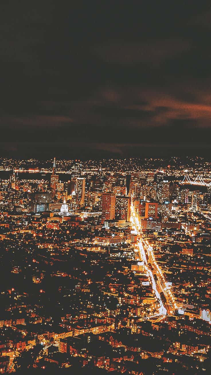 城市 桌布 壁紙 — 夜晚俯瞰廣闊城市，街道和建築物在陰暗多雲的天空下閃爍光芒。