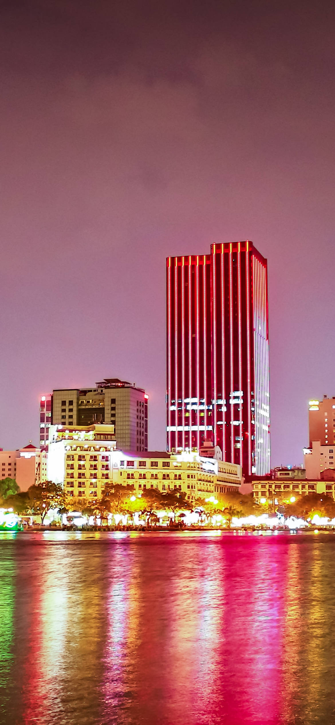 Ho Chi Minh City 桌布 壁紙 — 夜晚充滿活力的城市天際線，一座高聳的紅色燈光摩天大樓倒映在下方平靜的水面上。
