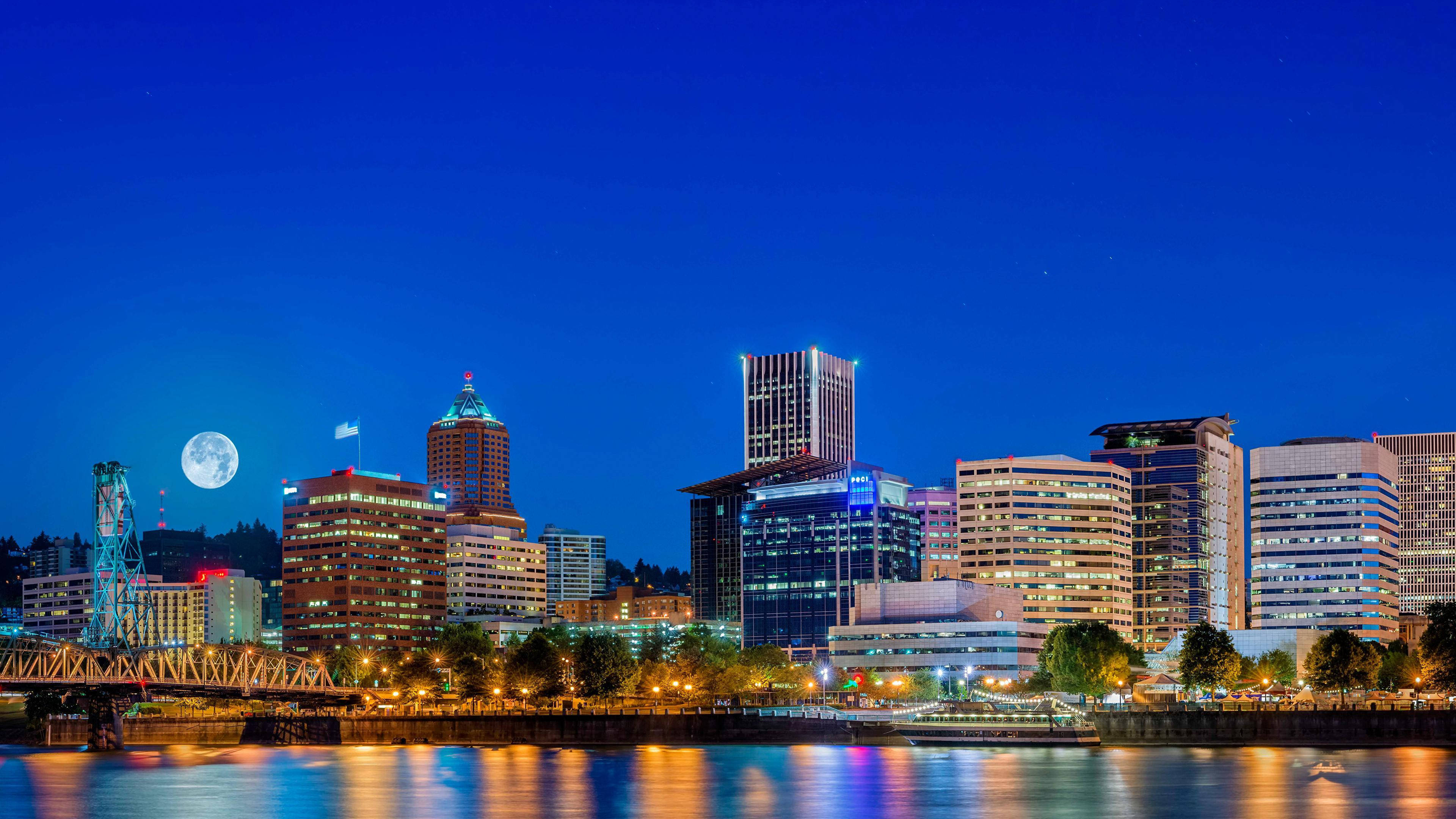 Portland 桌布 壁紙 — 夜晚充滿活力的城市天際線，滿月在燈火通明的摩天大樓上方閃耀，下方是反射的河流。