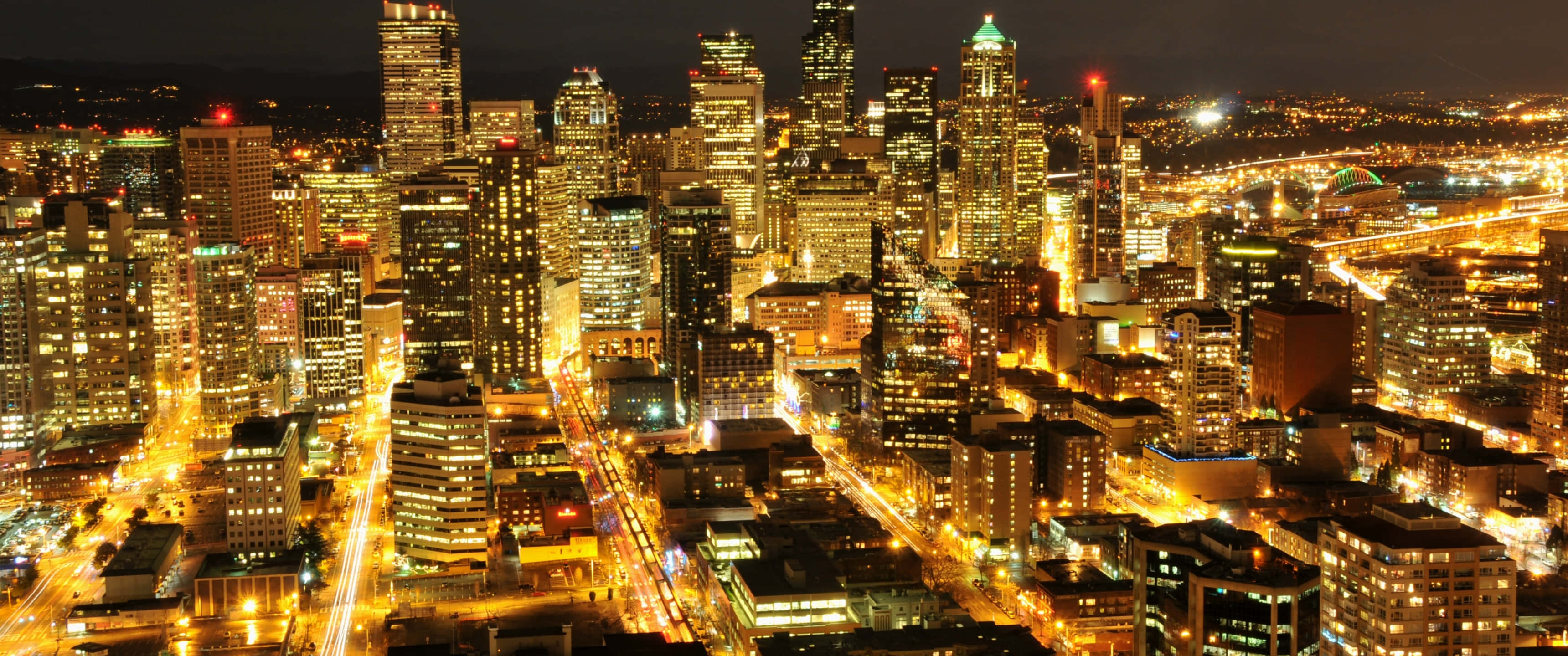 3440x1440p Seattle 桌布 壁紙 — 夜晚充滿活力的城市景觀鳥瞰圖，發光的摩天大樓和流動的交通燈照亮了城市範圍。