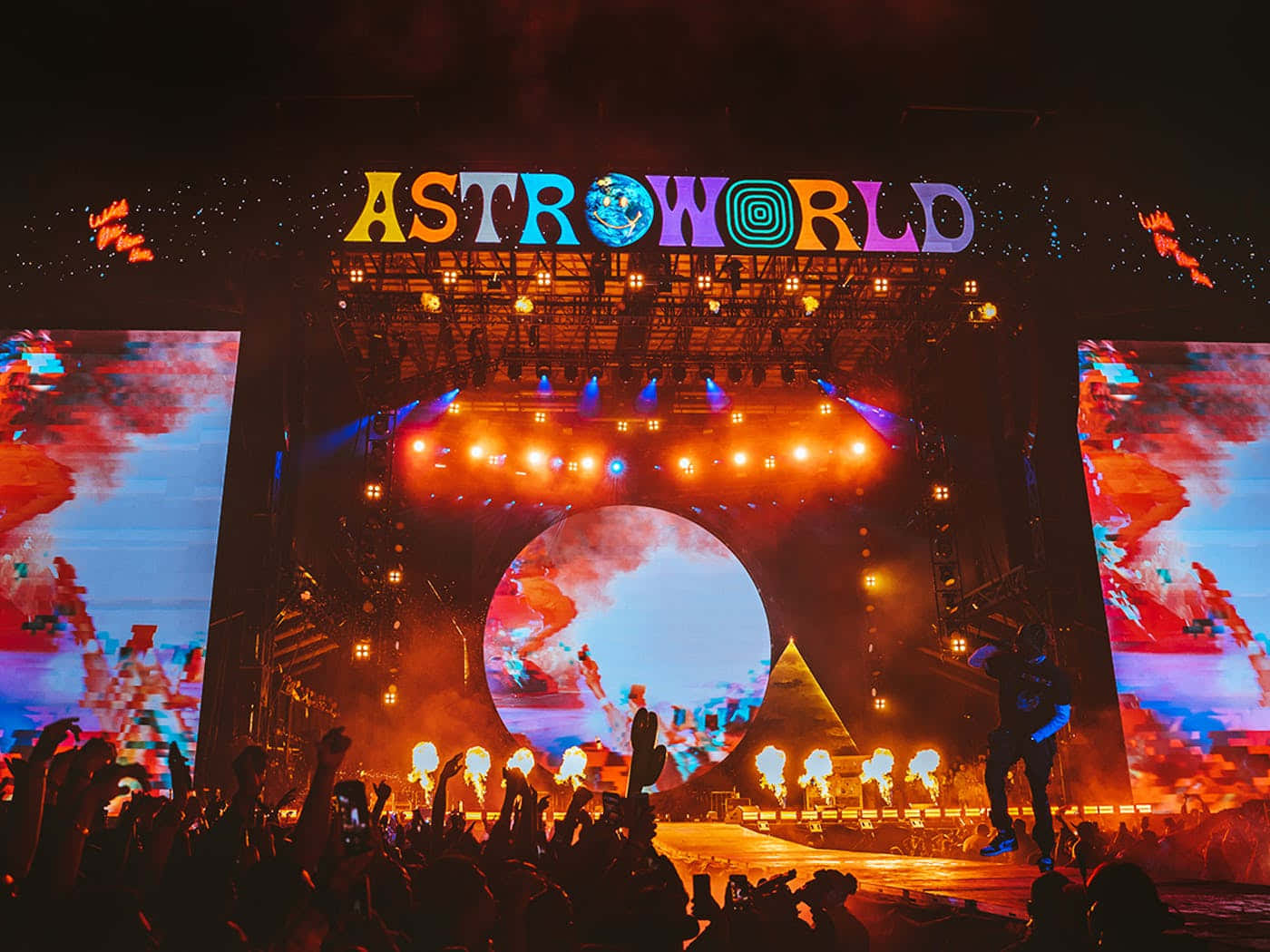 Astroworld 桌布 壁紙 — 夜晚充滿活力的演唱會舞台，'ASTROWORLD' 標誌在色彩繽紛的燈光下，在舉起雙手的剪影粉絲群上方閃耀。