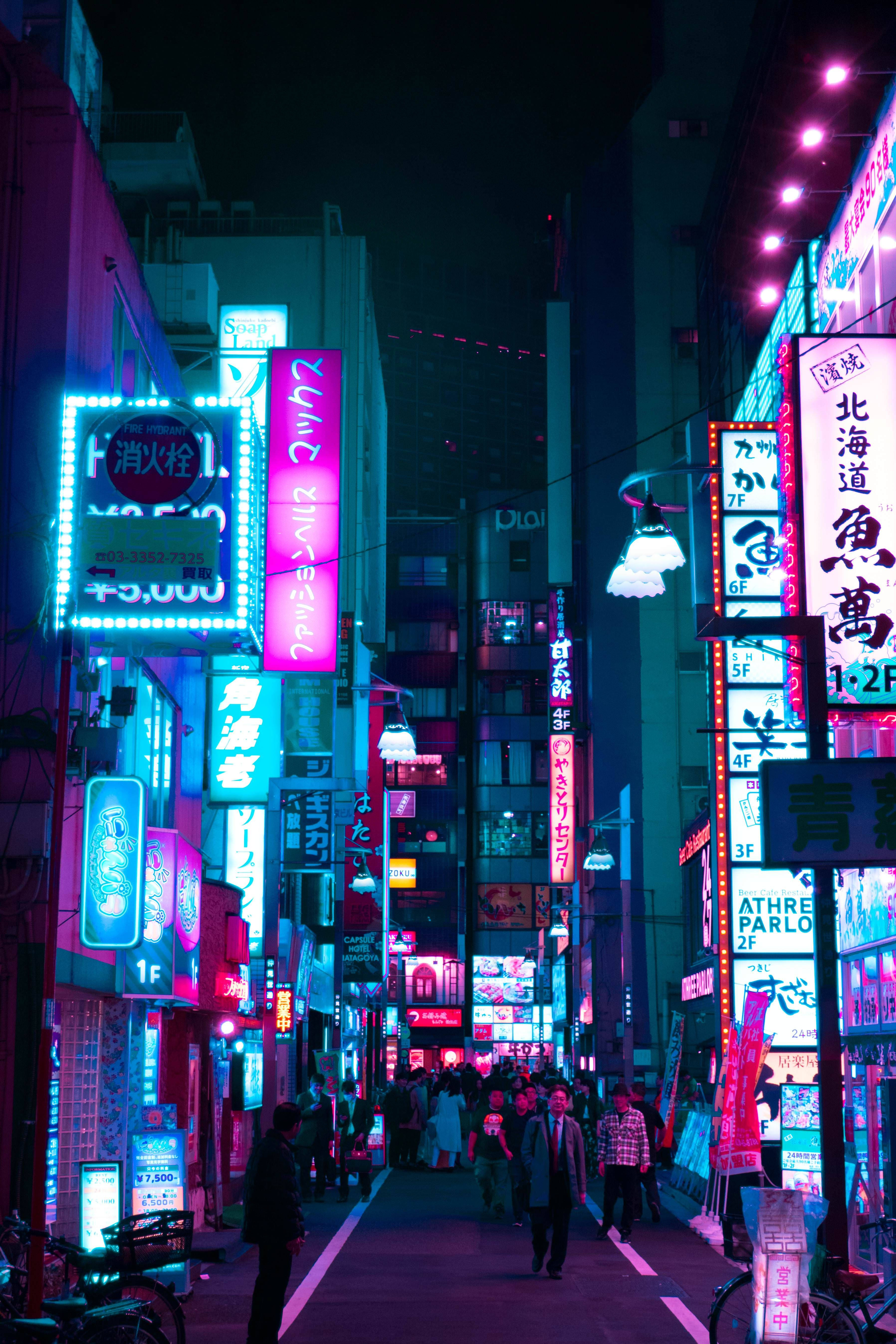 東京 桌布 壁紙 — 夜晚充滿活力的霓虹燈城市小巷，閃爍的招牌和在高樓大廈下行走的行人。