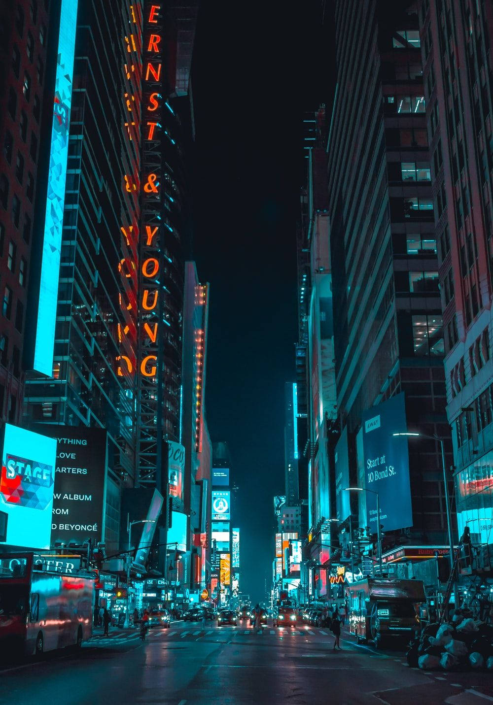 New York 桌布 壁紙 — 夜晚充滿活力的霓虹燈城市街道，高聳的摩天大樓和發光的廣告牌映照在潮濕的路面上。