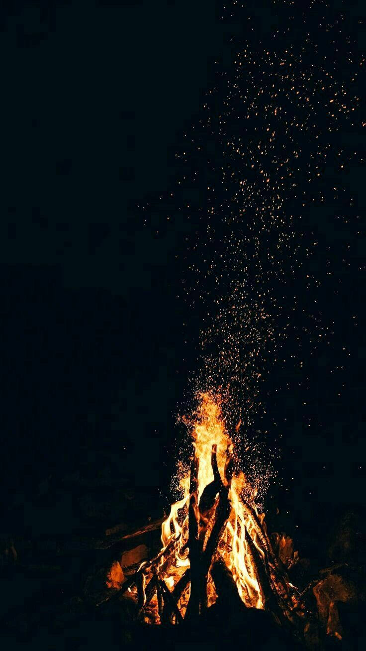 iPhone Fire 桌布 壁紙 — 夜晚咆哮的營火將明亮的橙色火花向上噴射，映襯著漆黑的天空。
