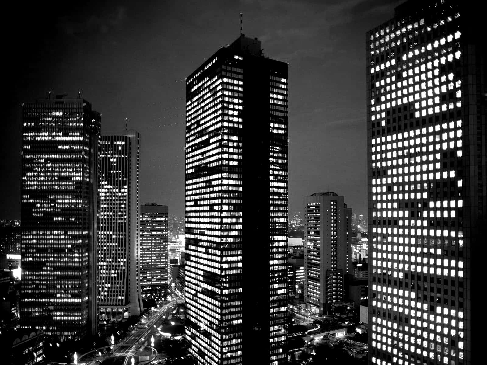 Buildings 桌布 壁紙 — 夜晚單色城市景觀，高聳的摩天大樓在黑暗的天空中閃爍著明亮的窗戶。