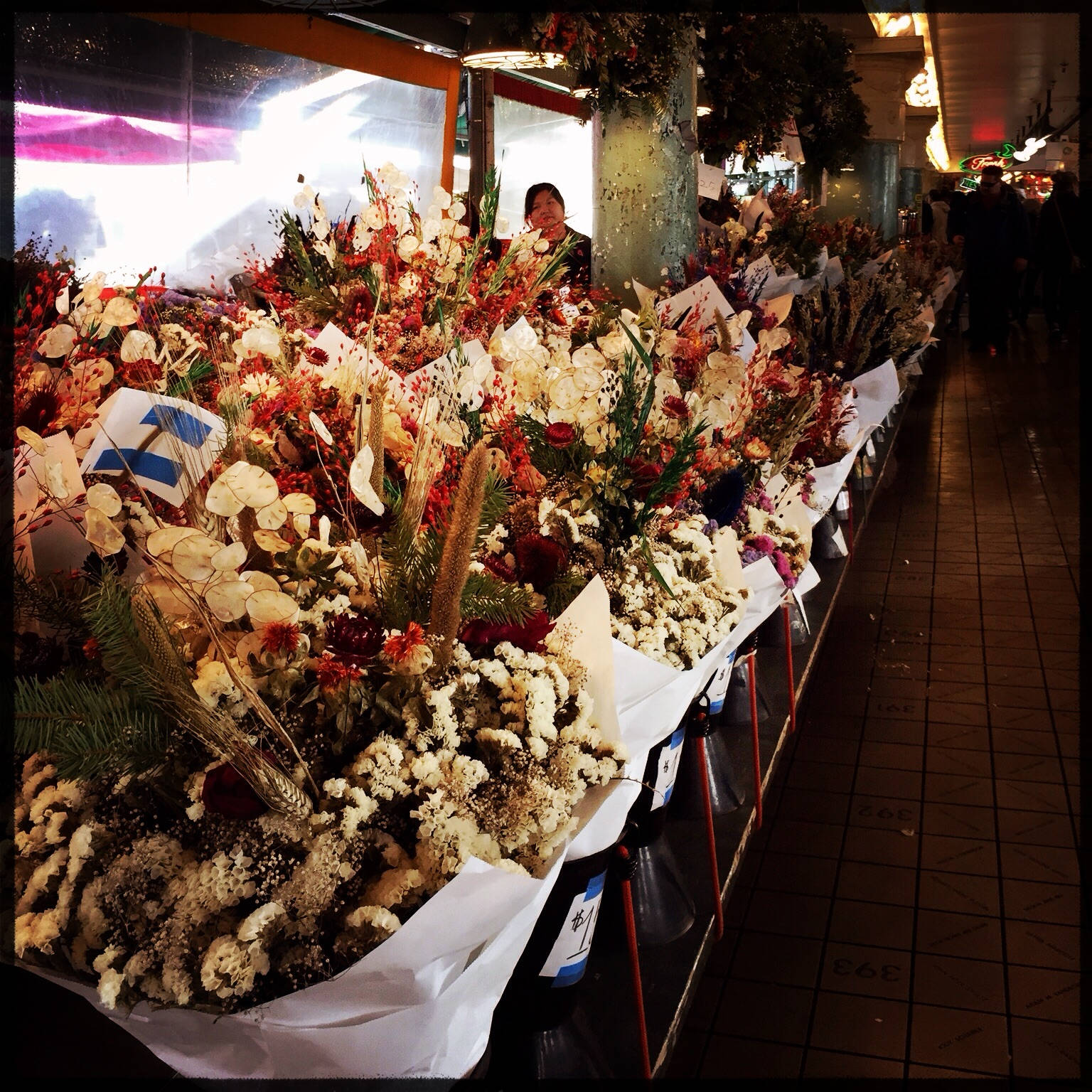 Pike Place Market 桌布 壁紙 — 夜晚在有蓋市場通道中展示的一長排鮮豔花卉佈置，並配有希臘國旗。