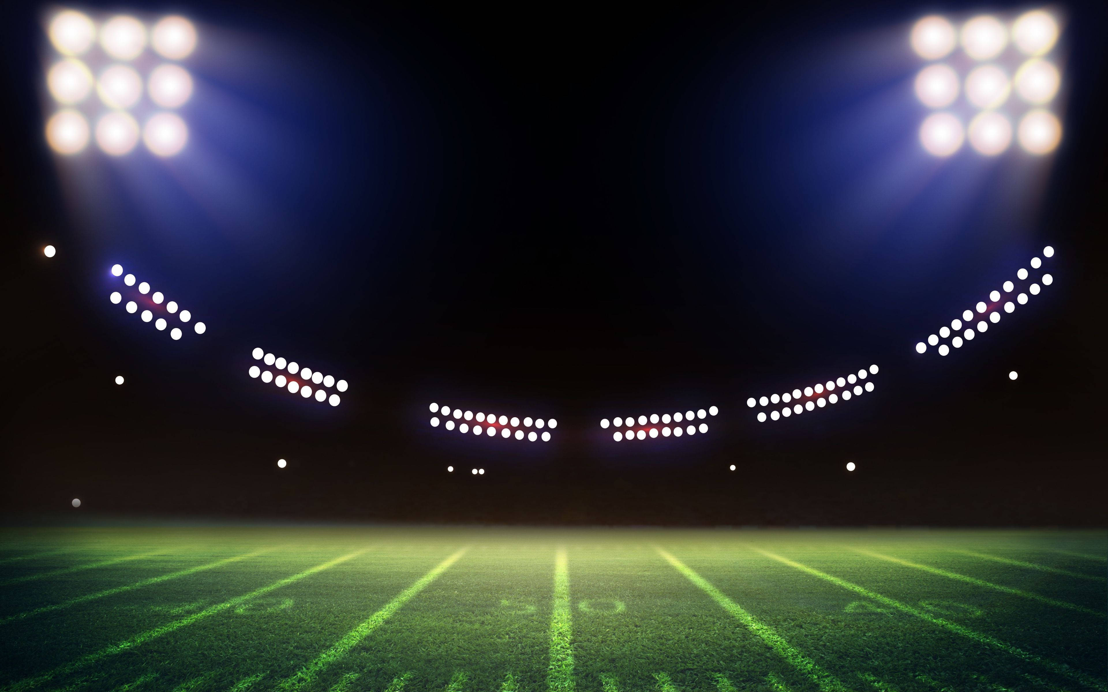Stadium 桌布 壁紙 — 夜晚在球場燈光下的明亮足球場，燈光在綠色草地上投射出戲劇性的光束。