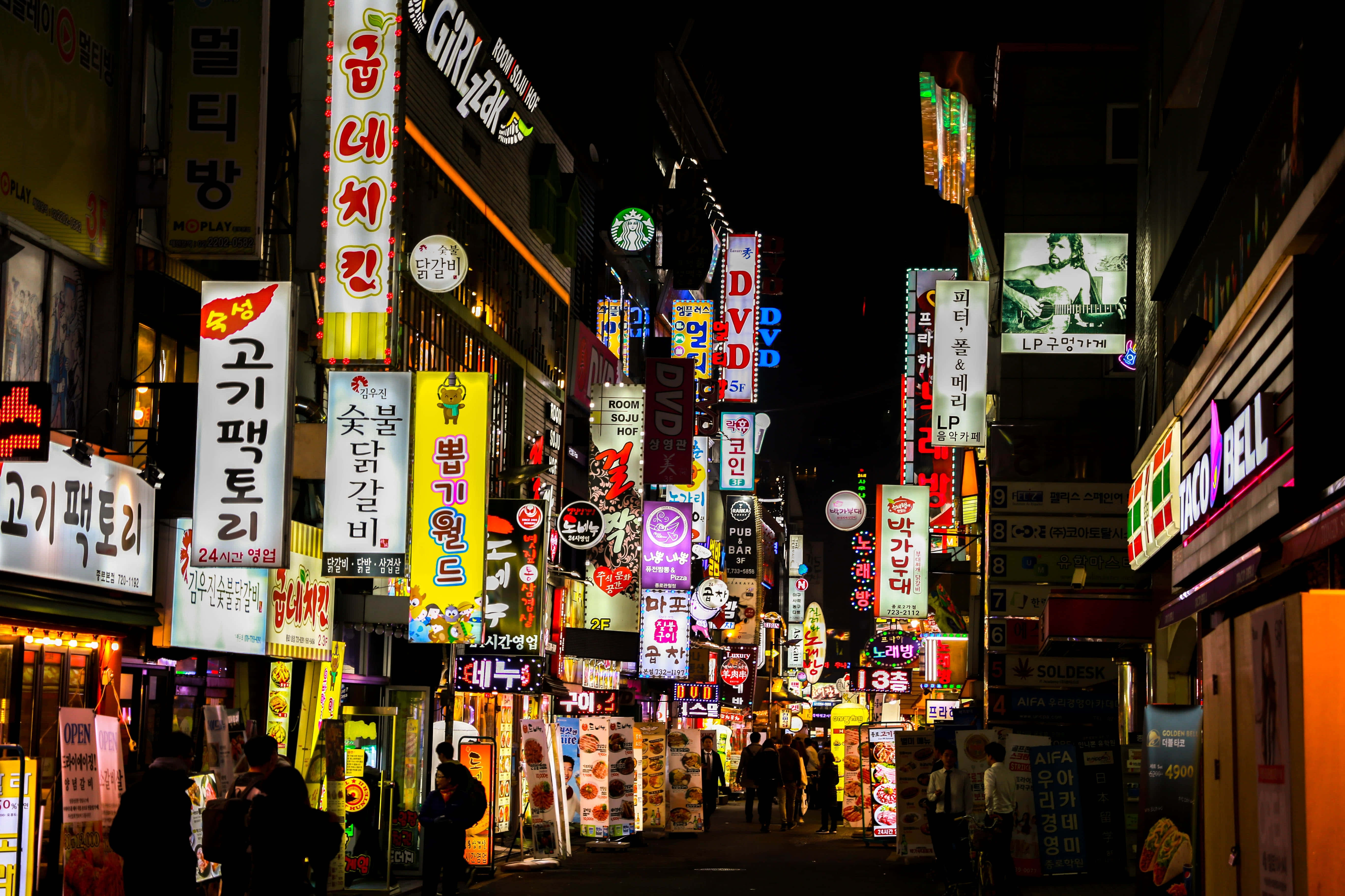 南韓 桌布 壁紙 — 夜晚在繁華的亞洲城市中，一條閃爍霓虹燈的小巷，有發光的招牌和行人剪影。