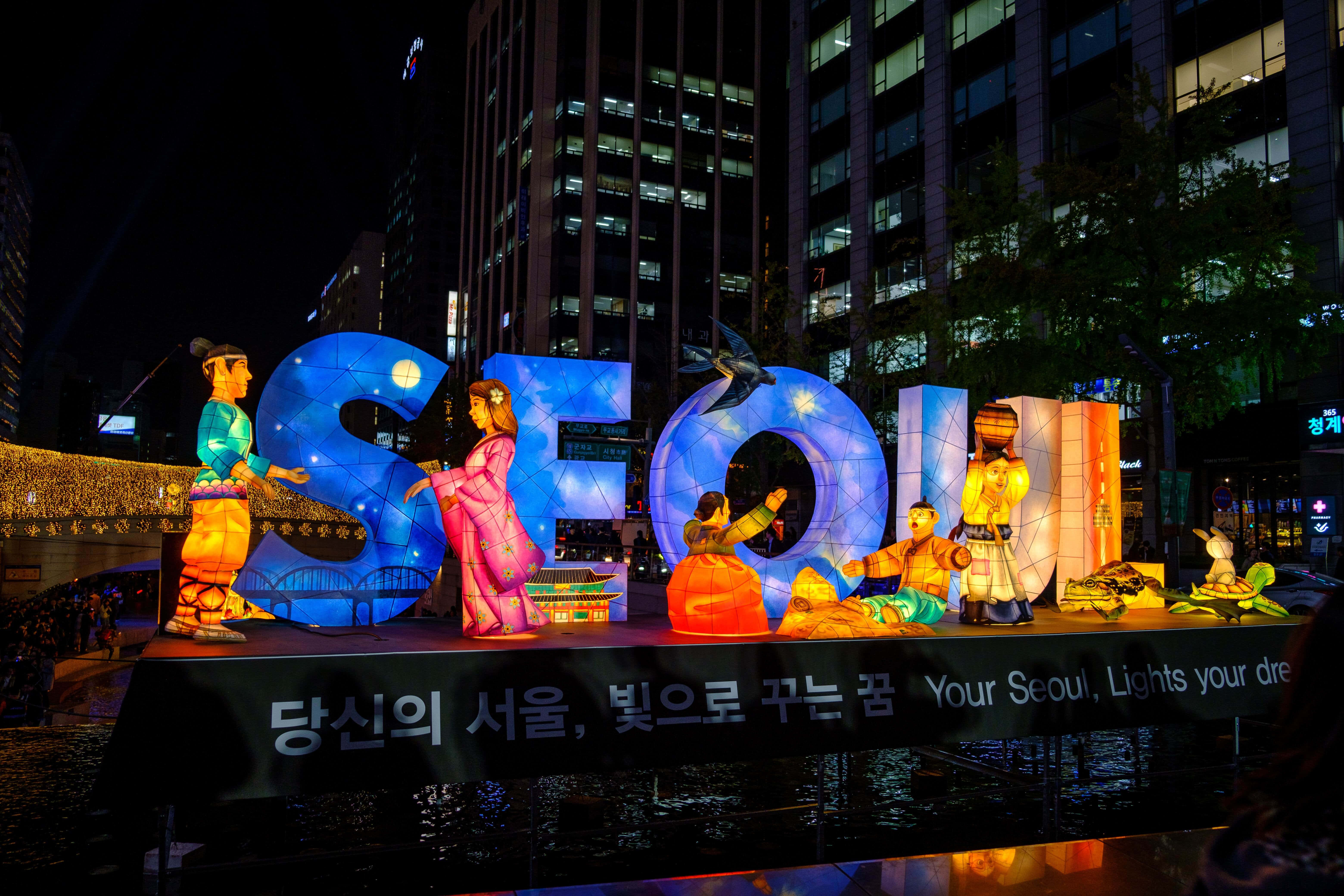 韓國 桌布 壁紙 — 夜晚城市廣場中，發光的藍色「SEOUL」字母與彩色燈籠造型一同亮起。