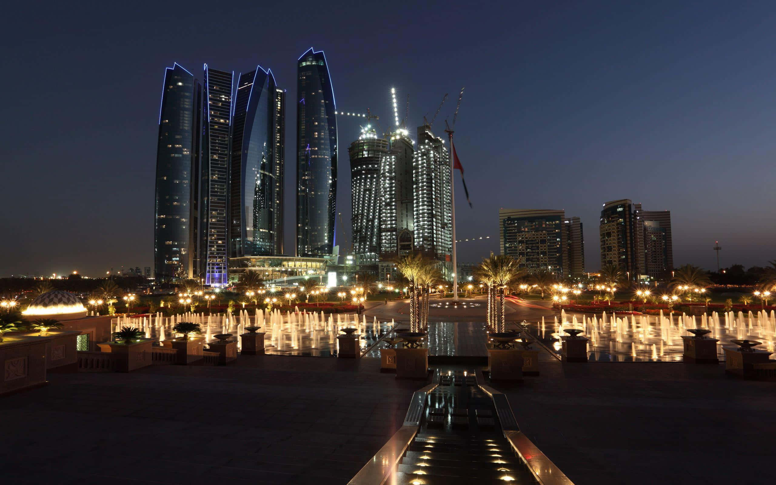 Uae 桌布 壁紙 — 夜晚城市景觀，以藍色霓虹燈點綴的摩天大樓倒映在噴泉廣場上。