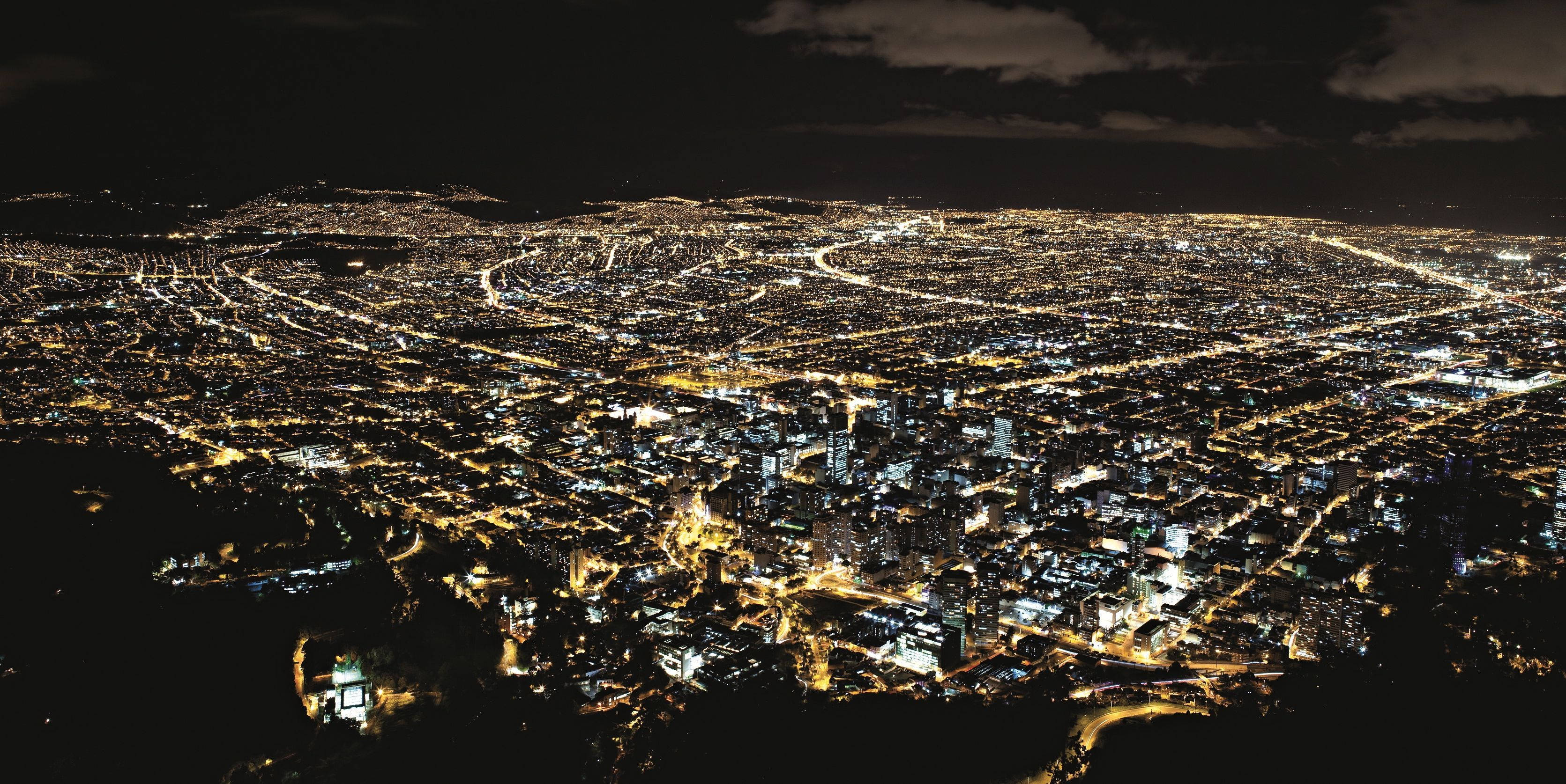 Bogota 桌布 壁紙 — 夜晚城市鳥瞰圖，黑暗多雲的天空下，發光的街道和建築物延伸開來。