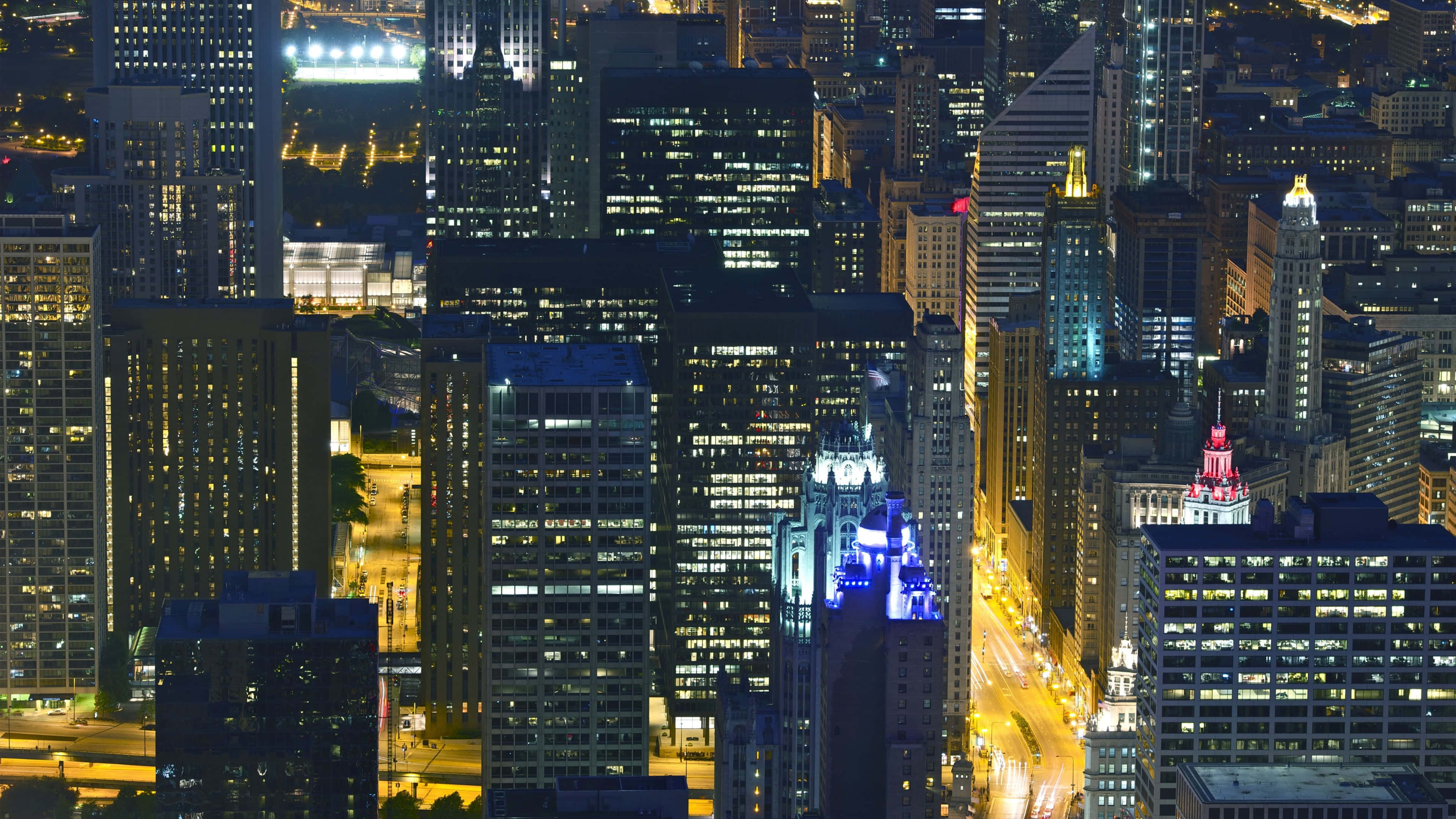 4K Ultra HD Chicago 桌布 壁紙 — 夜晚密集城市景觀的鳥瞰圖，下方有燈火通明的摩天大樓和發光的街道。