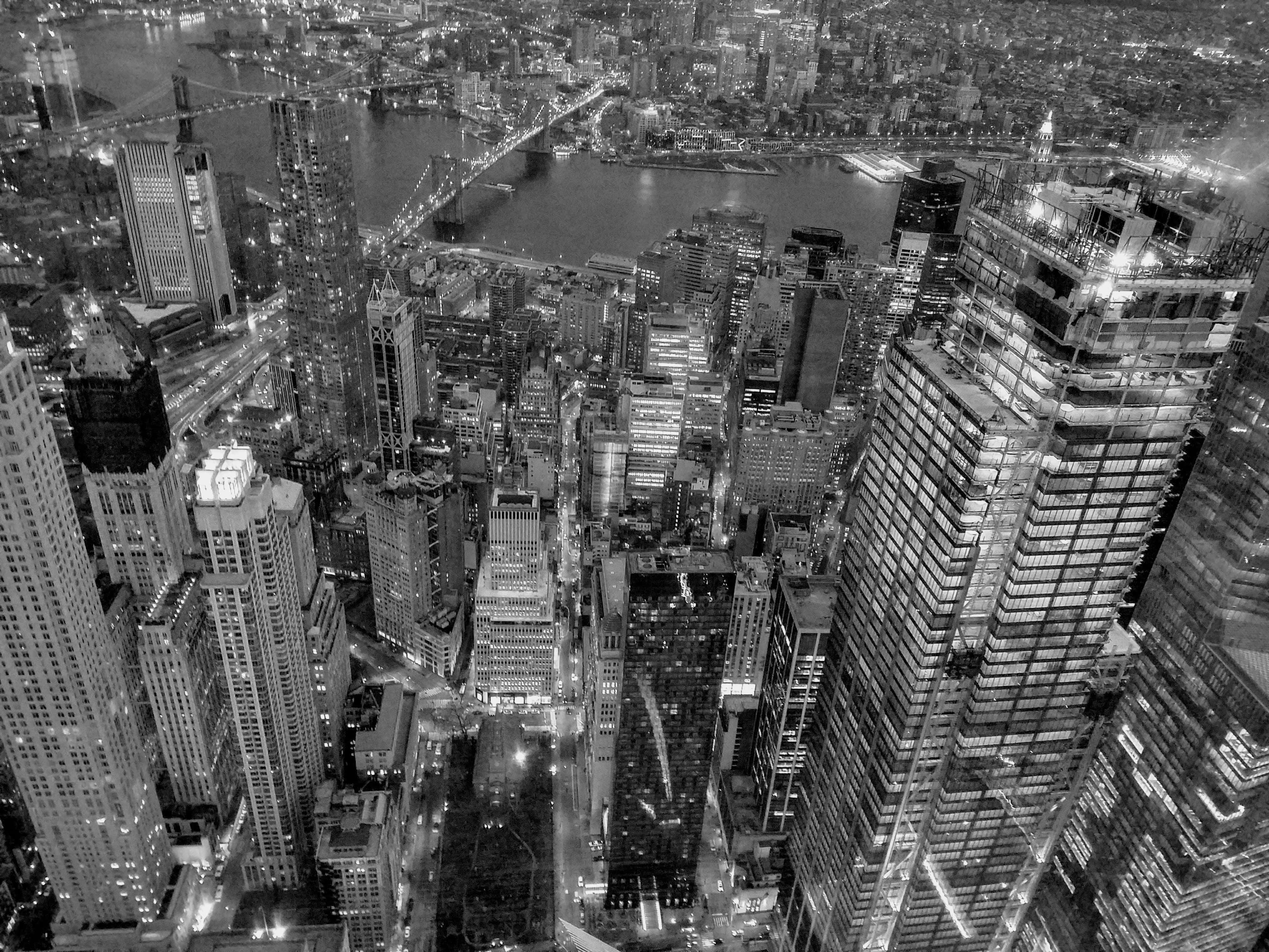 Black And White Cityscape 桌布 壁紙 — 夜晚密集城市景觀的黑白空拍圖，帶有發光的摩天大樓和水面上的橋樑。