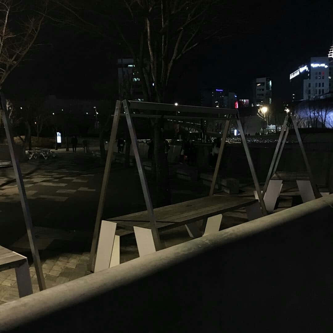 暗黑風格 桌布 壁紙 — 夜晚寧靜的城市公園，空蕩蕩的鞦韆和遠處的城市燈光在黑暗的樹木間閃爍。