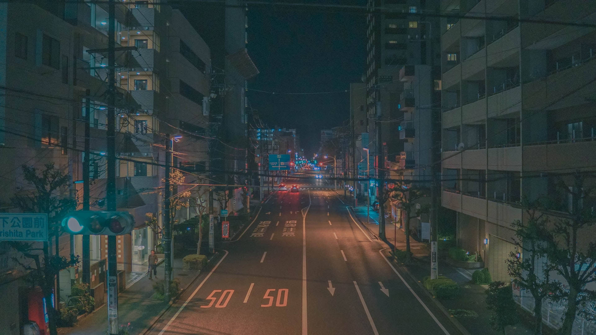Road 桌布 壁紙 — 夜晚寧靜的城市街道，發光的街燈和遠處的車頭燈照亮高樓之間的道路。