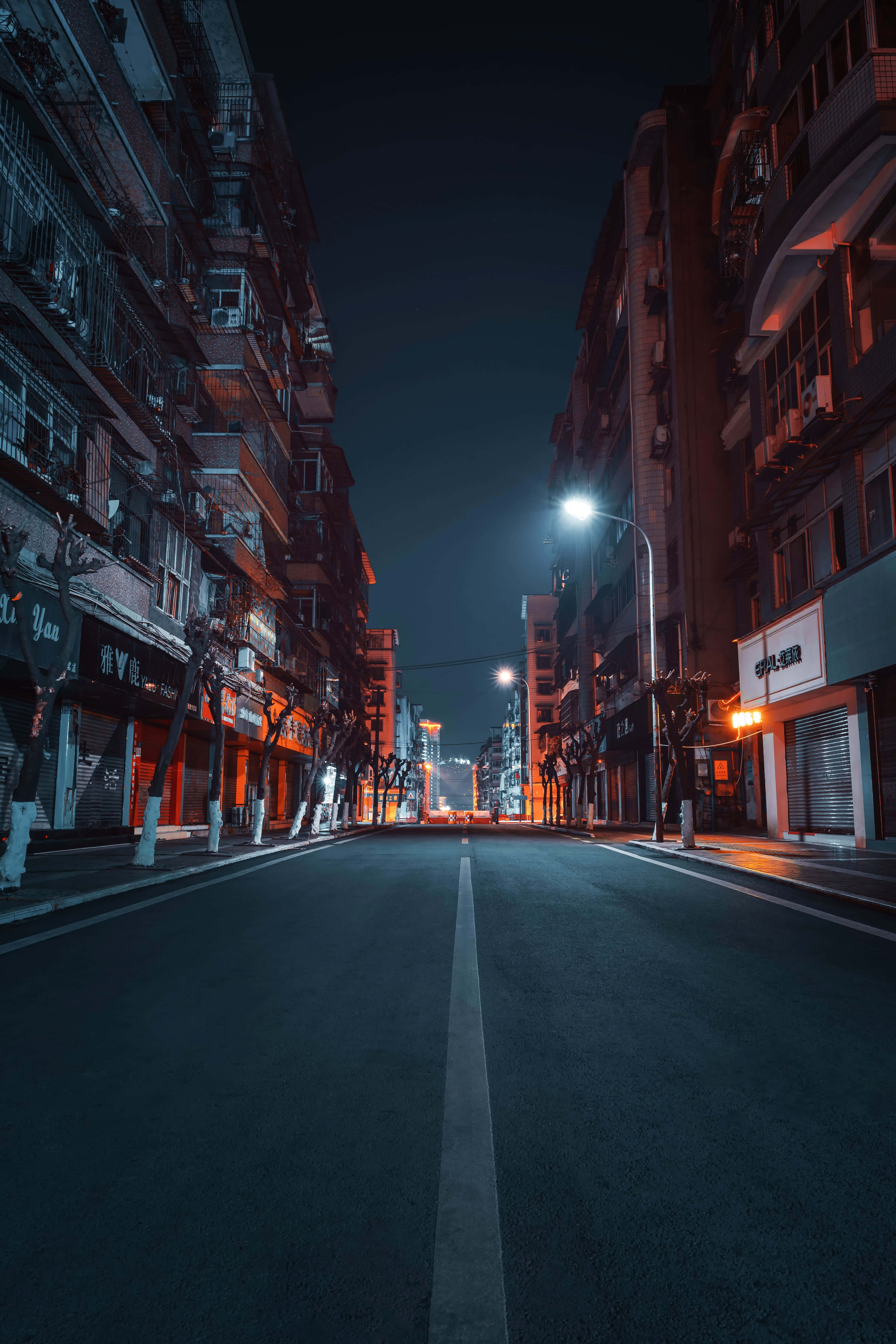 Street 桌布 壁紙 — 夜晚寧靜的城市街道，發光的街燈在高層住宅樓之間潮濕的路面上投射出溫暖的橙色倒影。