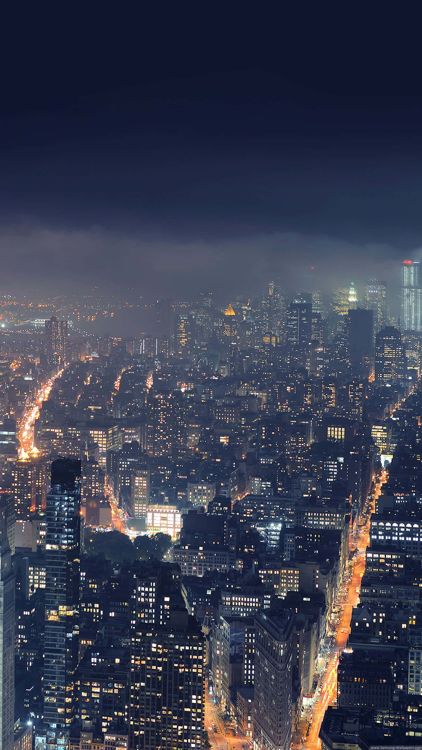 鎖屏 桌布 壁紙 — 夜晚廣闊城市的鳥瞰圖，在黑暗多雲的天空下，閃爍的摩天大樓和燈火通明的街道。