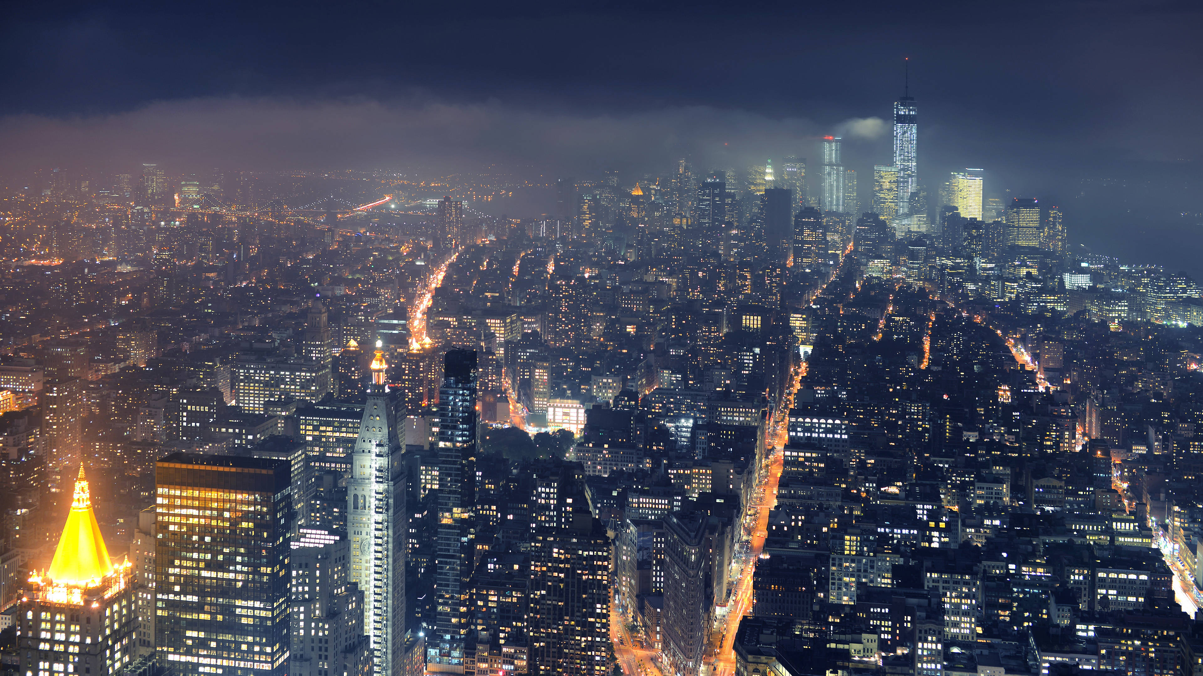 City Night 桌布 壁紙 — 夜晚廣闊城市的鳥瞰圖，在黑暗多雲的天空下，閃爍的摩天大樓和燈火通明的街道。
