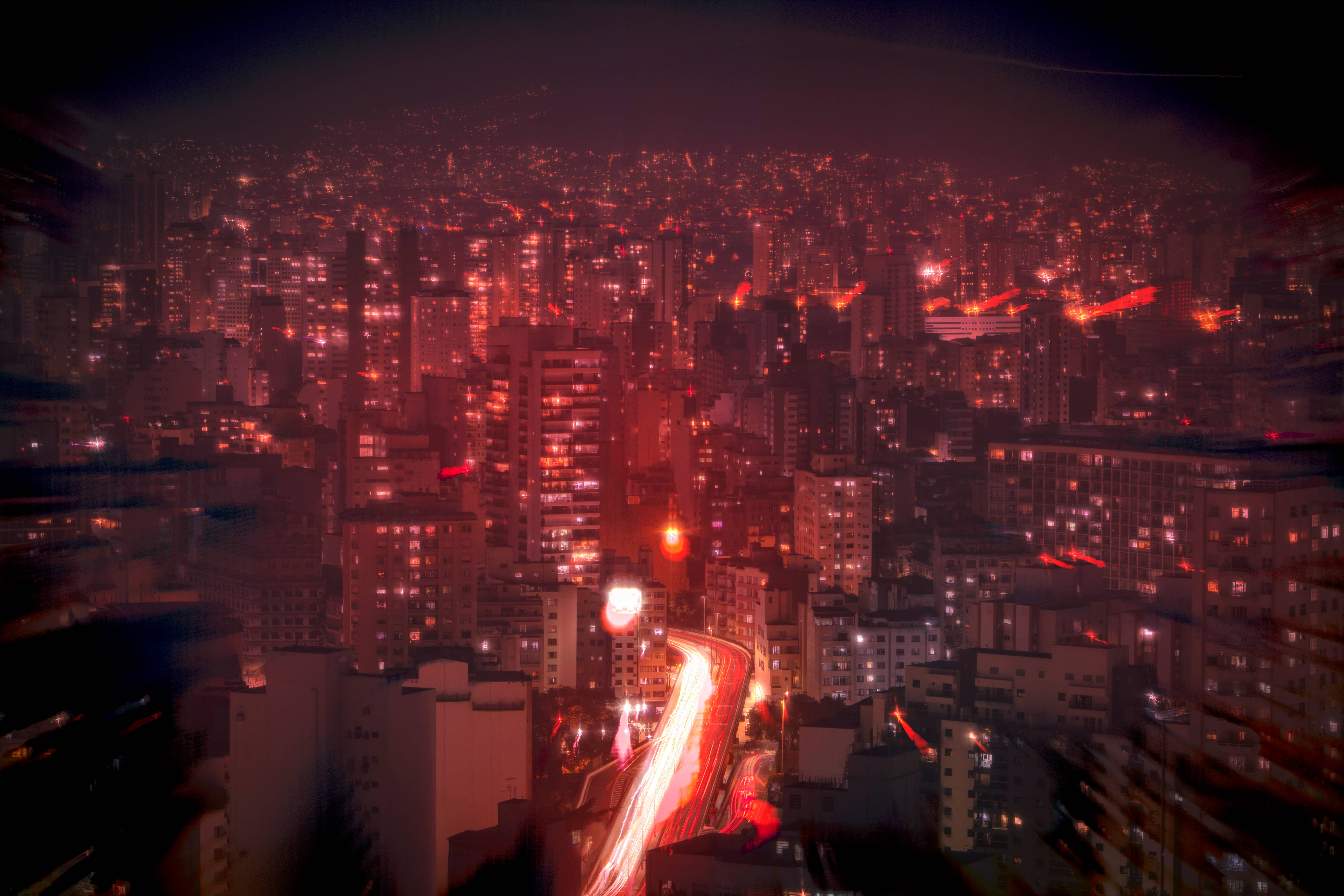 Red Color 桌布 壁紙 — 夜晚廣闊城市的鳥瞰圖，帶有發光的紅燈和流動的交通痕跡。