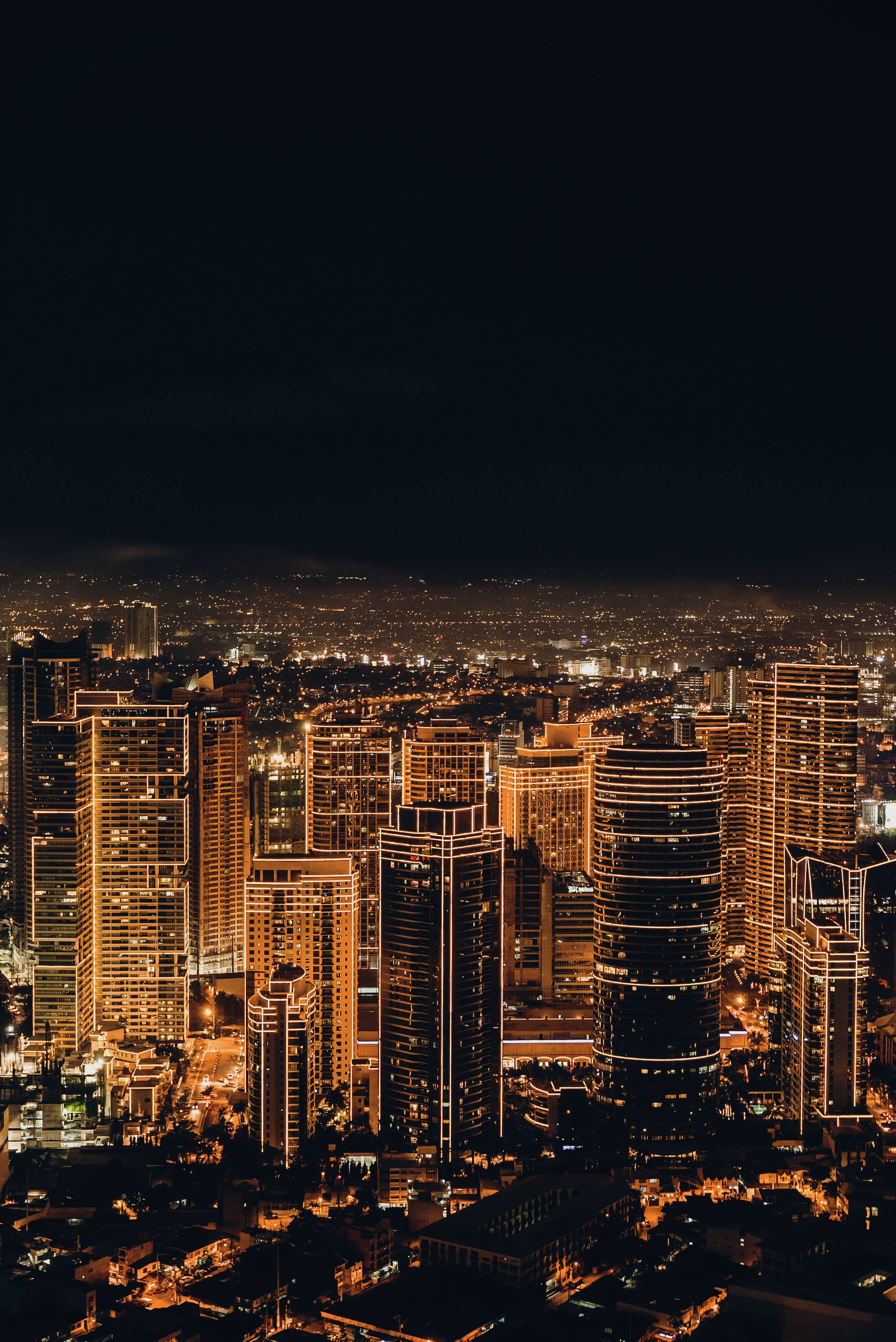 夜空 桌布 壁紙 — 夜晚廣闊城市的鳥瞰圖，摩天大樓閃爍著溫暖的金色燈光，映襯著黑暗的天空。