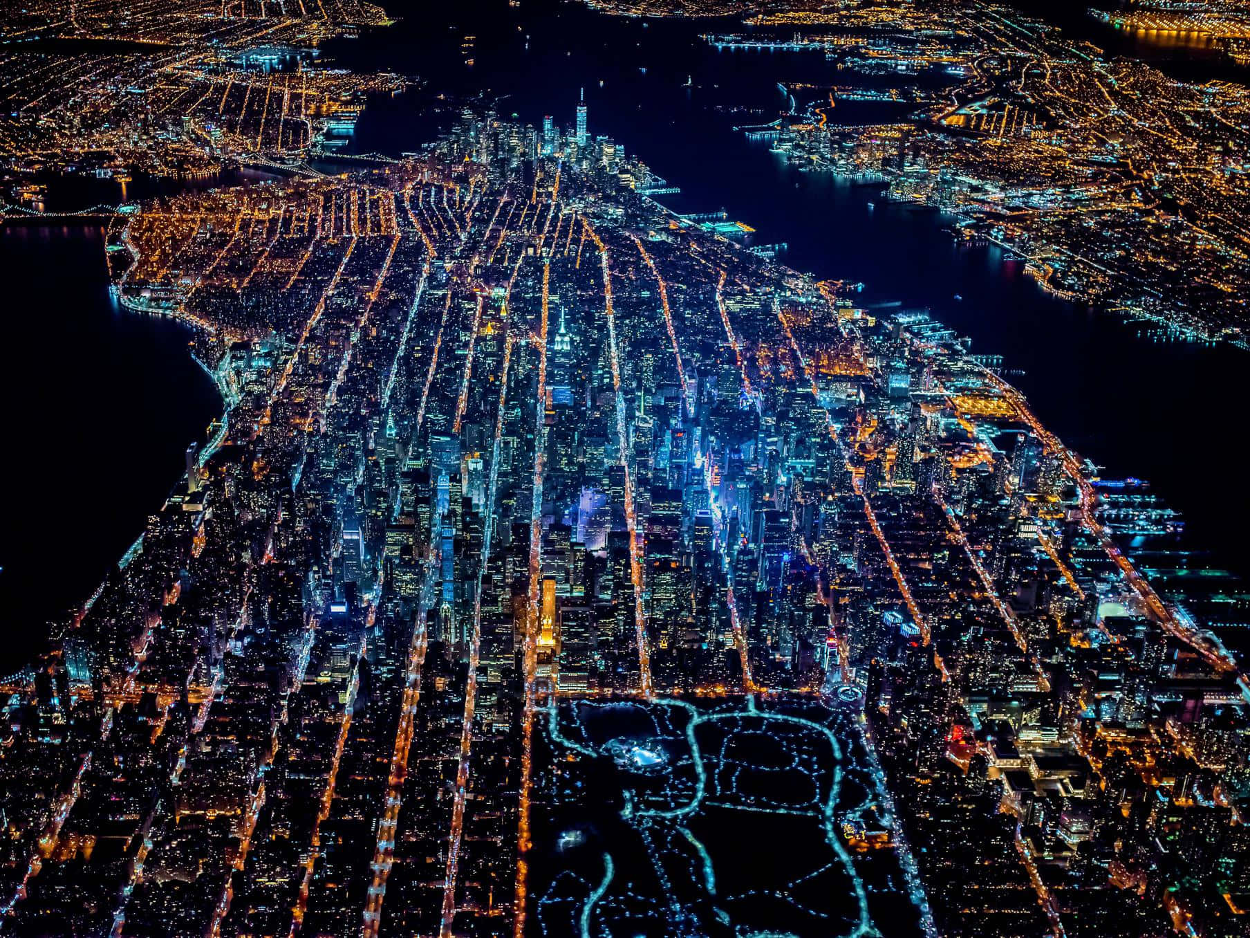 紐約市 桌布 壁紙 — 夜晚廣闊城市的鳥瞰圖，發光的街道和建築物在黑暗的水面上照亮。