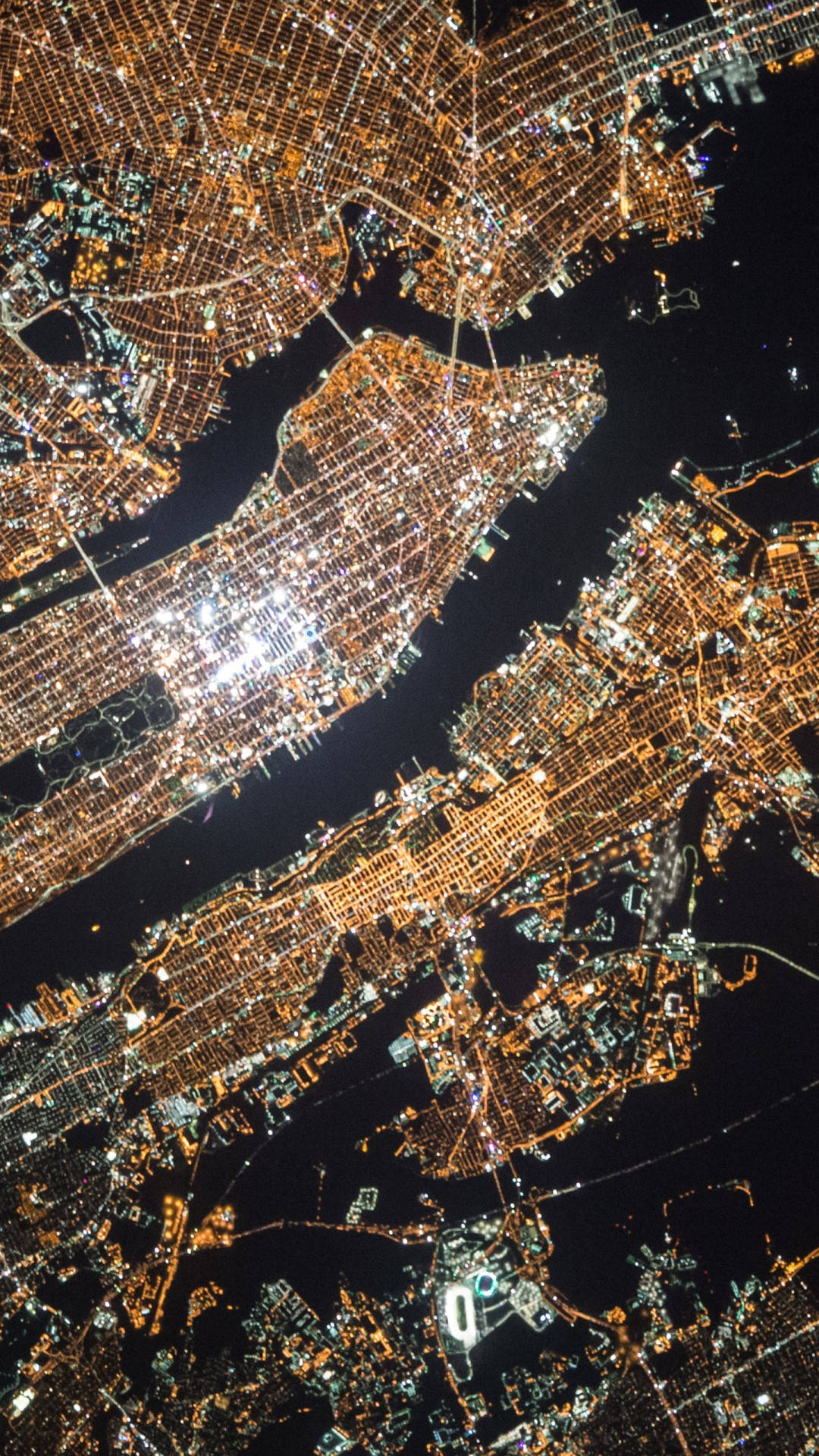 new york city iPhone x 桌布 壁紙 — 夜晚廣闊城市的鳥瞰圖，金色燈光照亮密集的城市網格和水道。